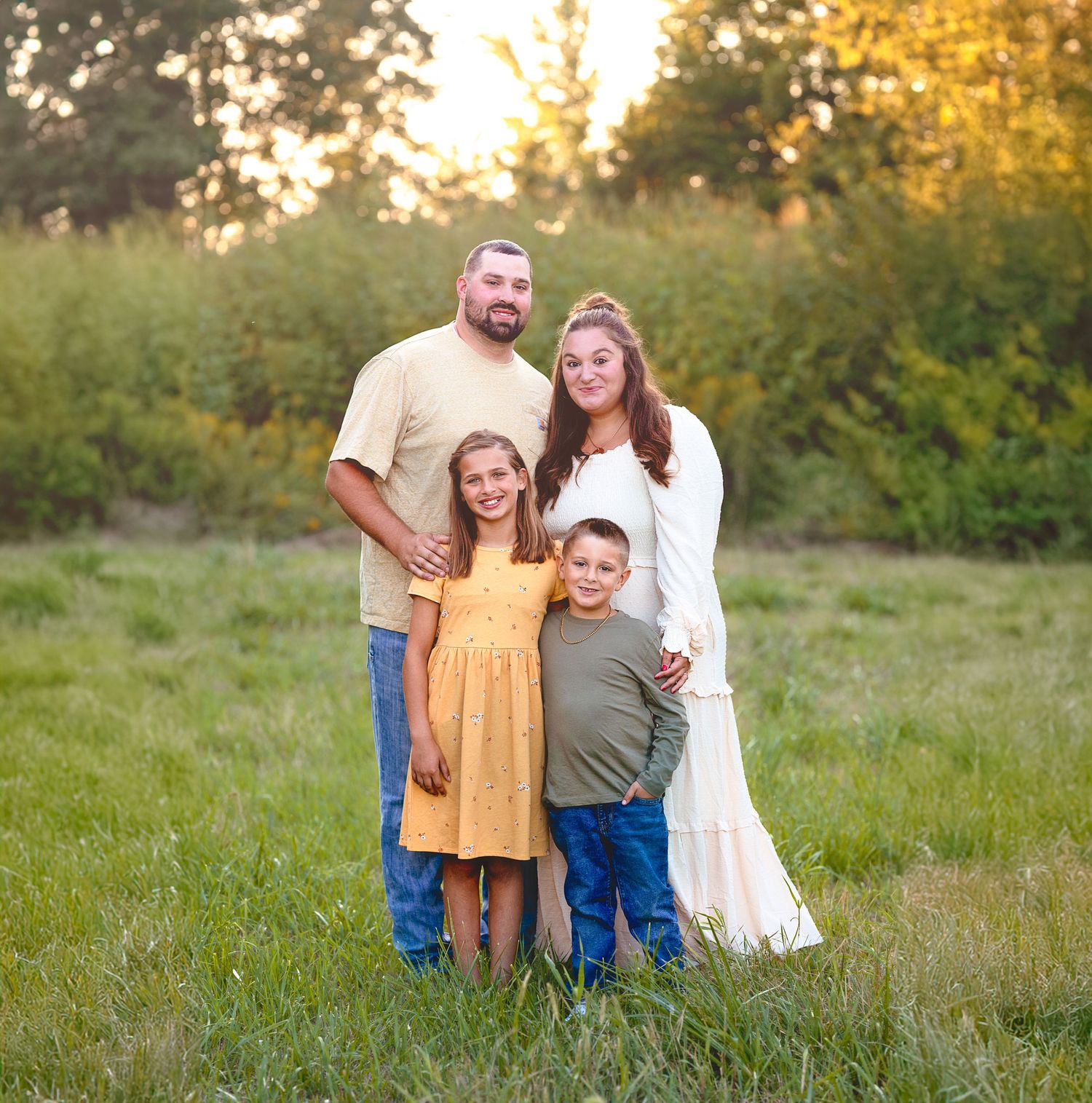 Family of four posing together outdoors during golden hour in natural field setting.