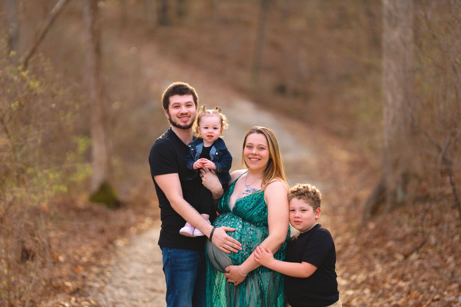 A family portrait outdoors featuring a woman in a green dress and children on a forest path.