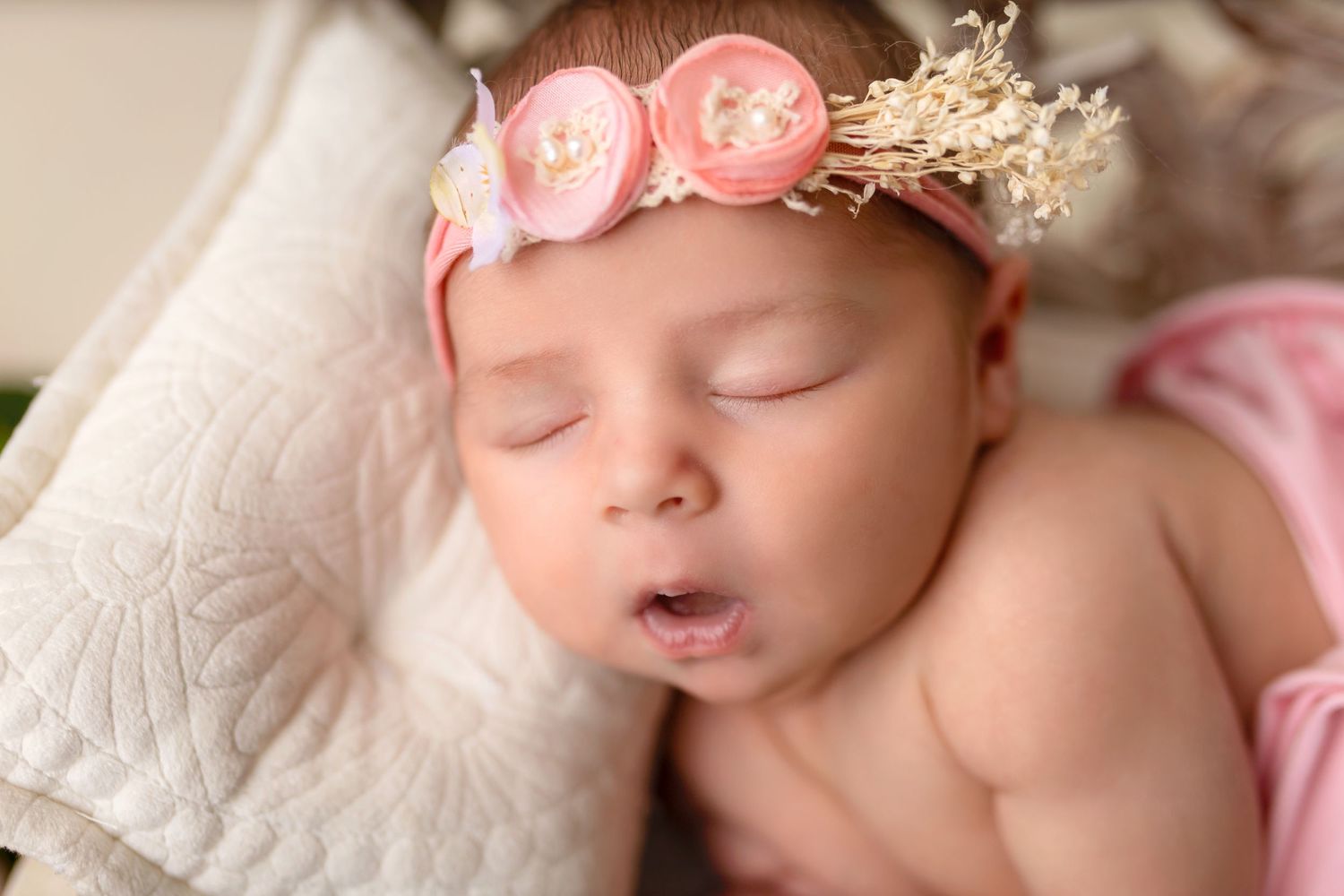 Sleeping newborn with pink floral crown on white pillow.