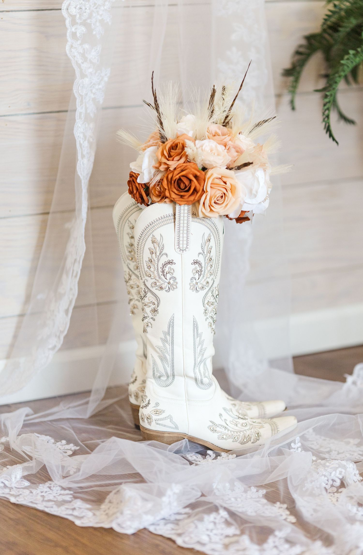 White decorative cowboy boot vase filled with peach and orange roses and flowers on lace tablecloth.