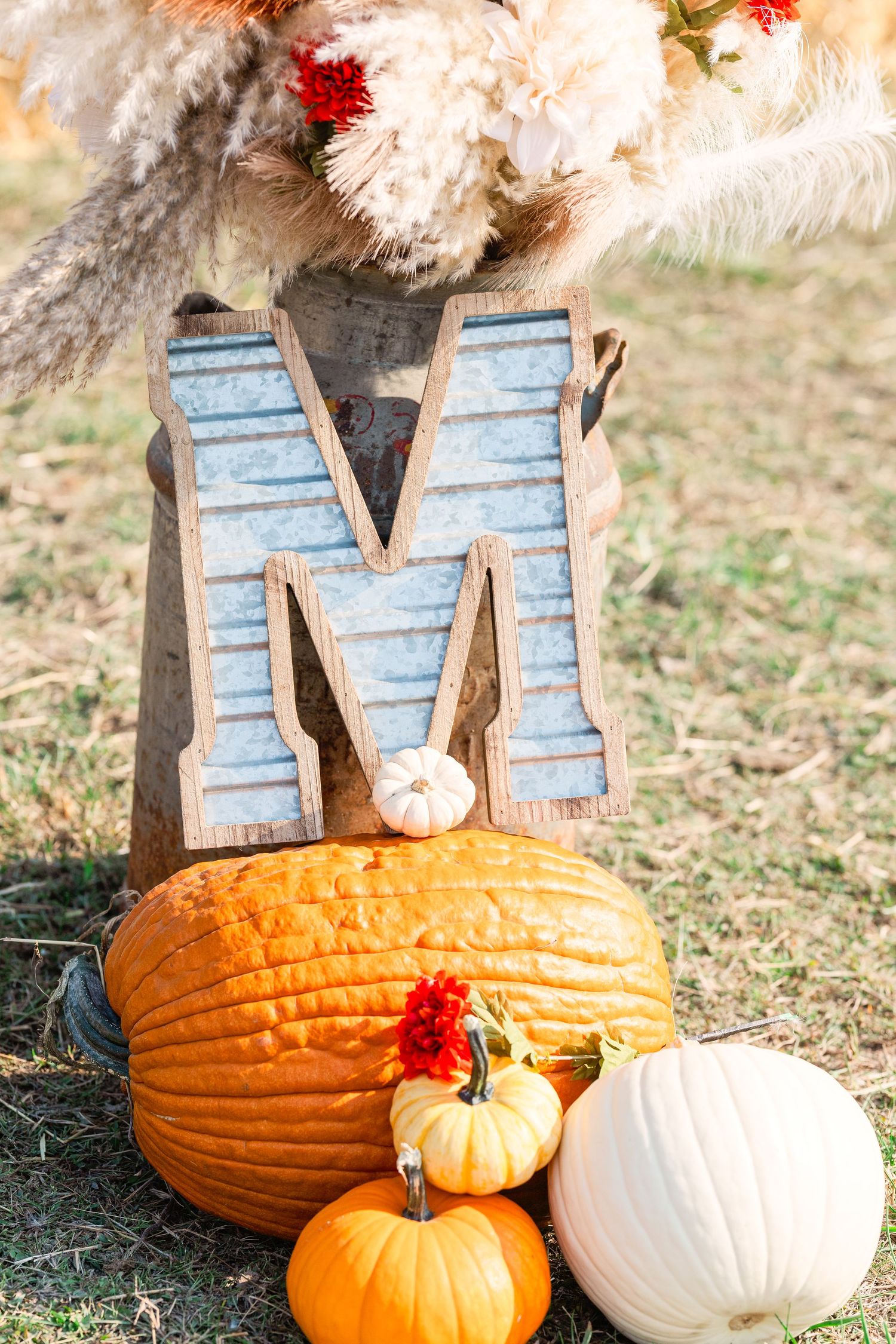 Fall wedding decor featuring a blue metal letter M with pumpkins and dried flowers.