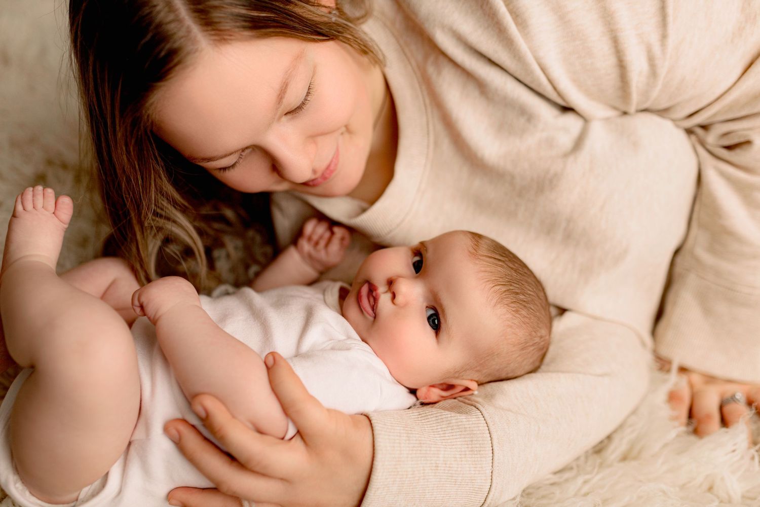 A tender bonding moment between parent and baby lying together on soft beige fabric.