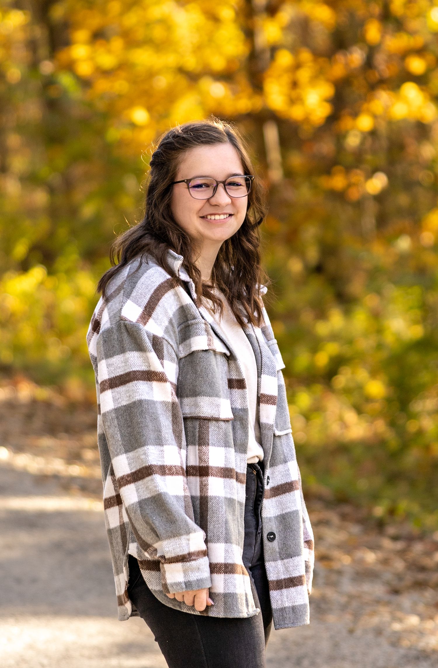 Fall portrait with plaid shacket against vibrant yellow autumn leaves.