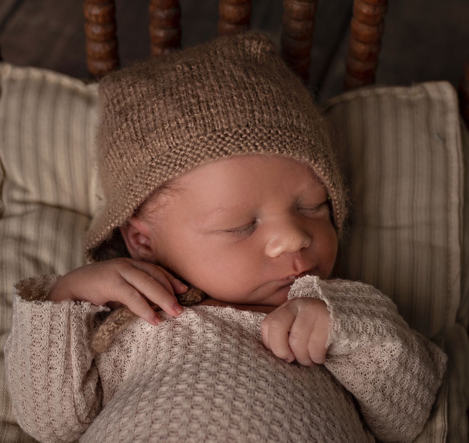 Close-up of sleeping baby in brown knit hat and sweater on striped pillow.