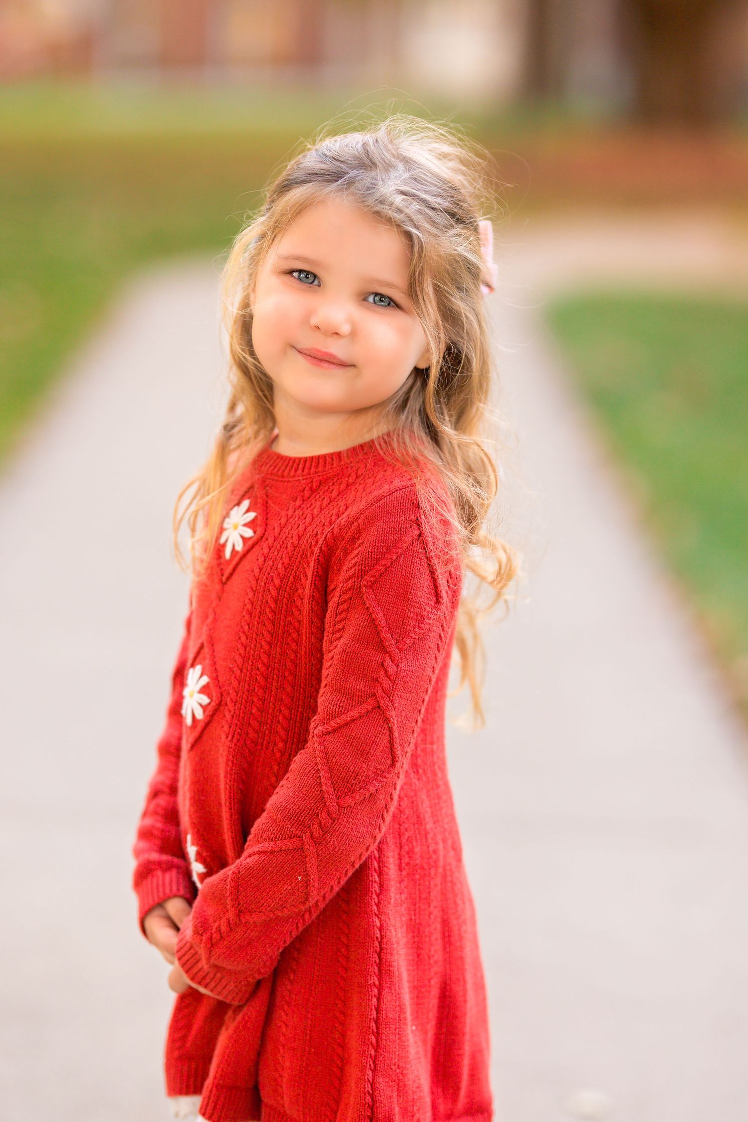 Portrait of person in bright red knit sweater dress standing on sidewalk.