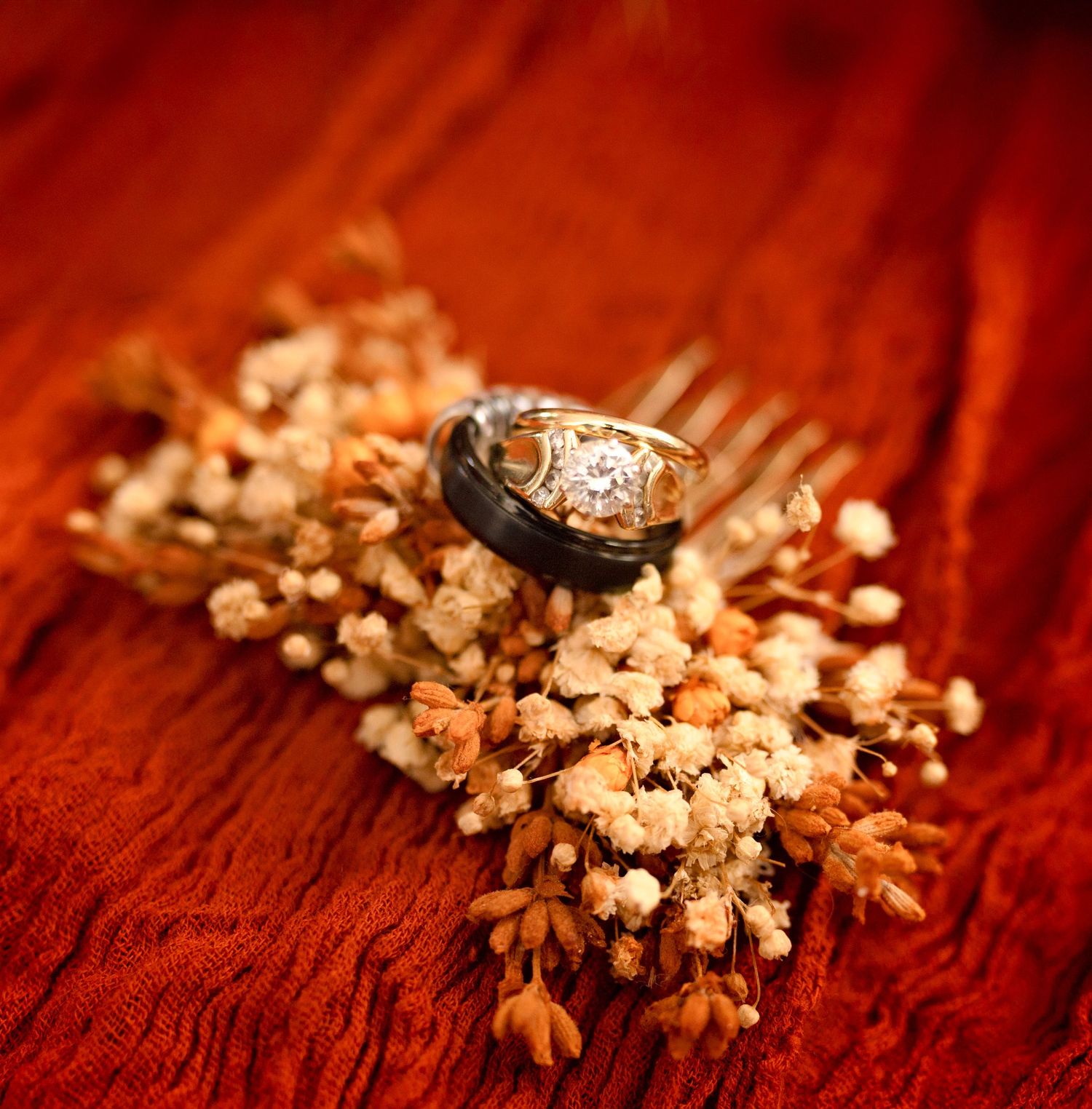 Wedding rings displayed on dried flowers against a rich wooden surface.