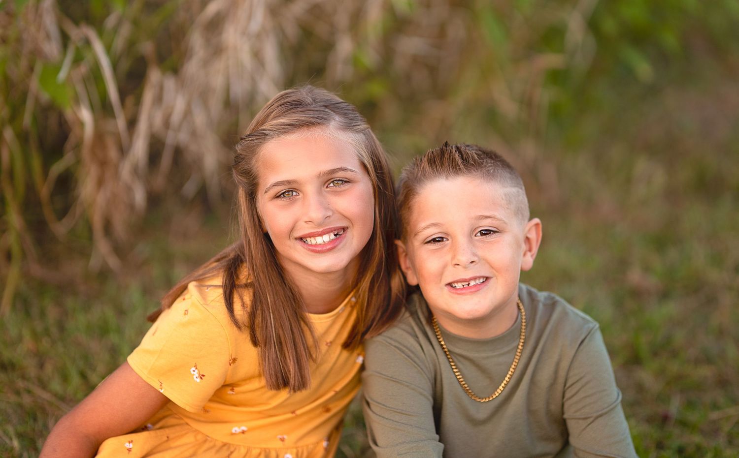 Two siblings smiling outdoors in casual clothing during golden hour photography session.