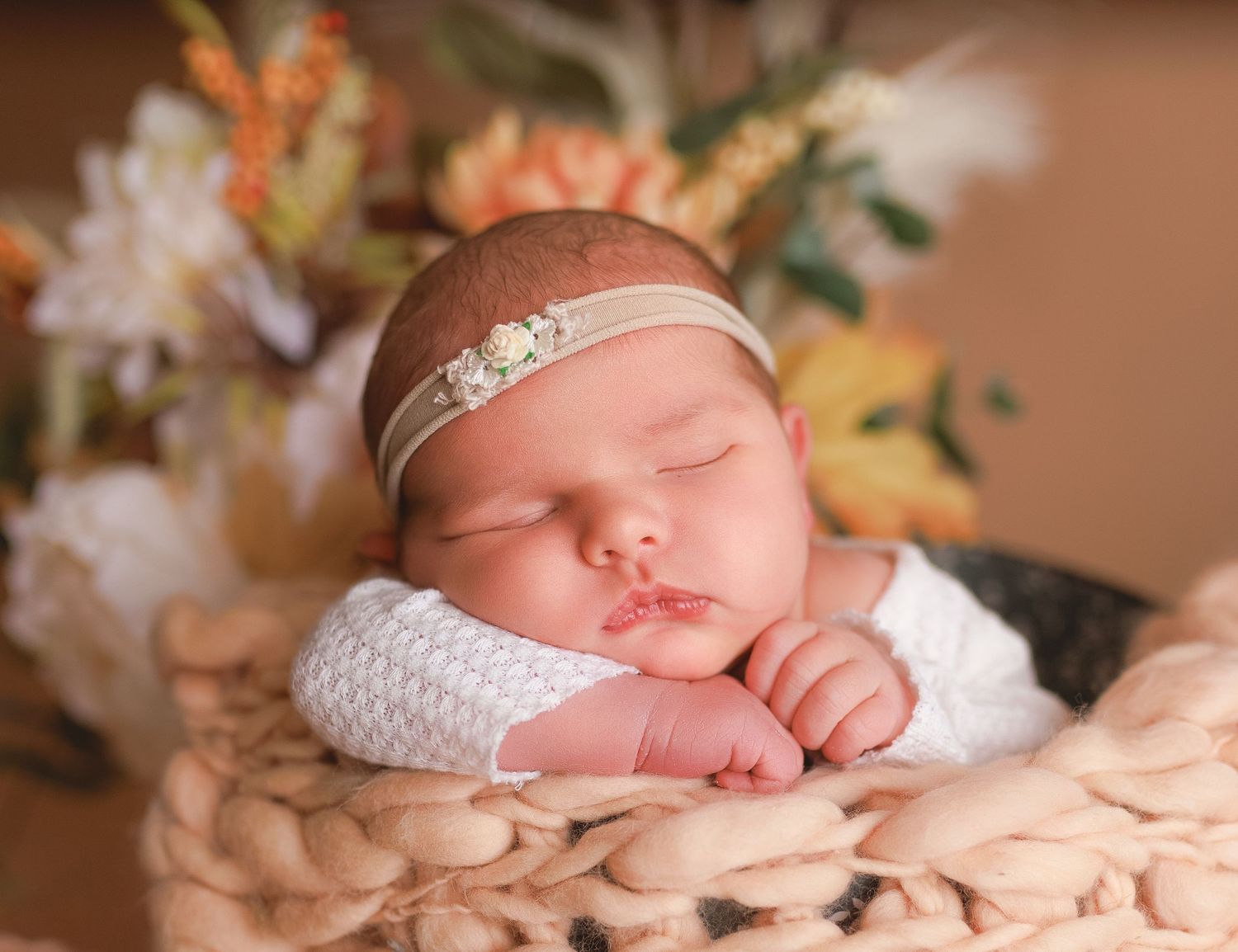 Sleeping newborn wearing delicate headband posed with autumn flowers.