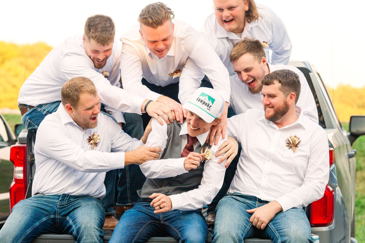 A group of friends in white shirts share laughs while sitting in the back of a truck.