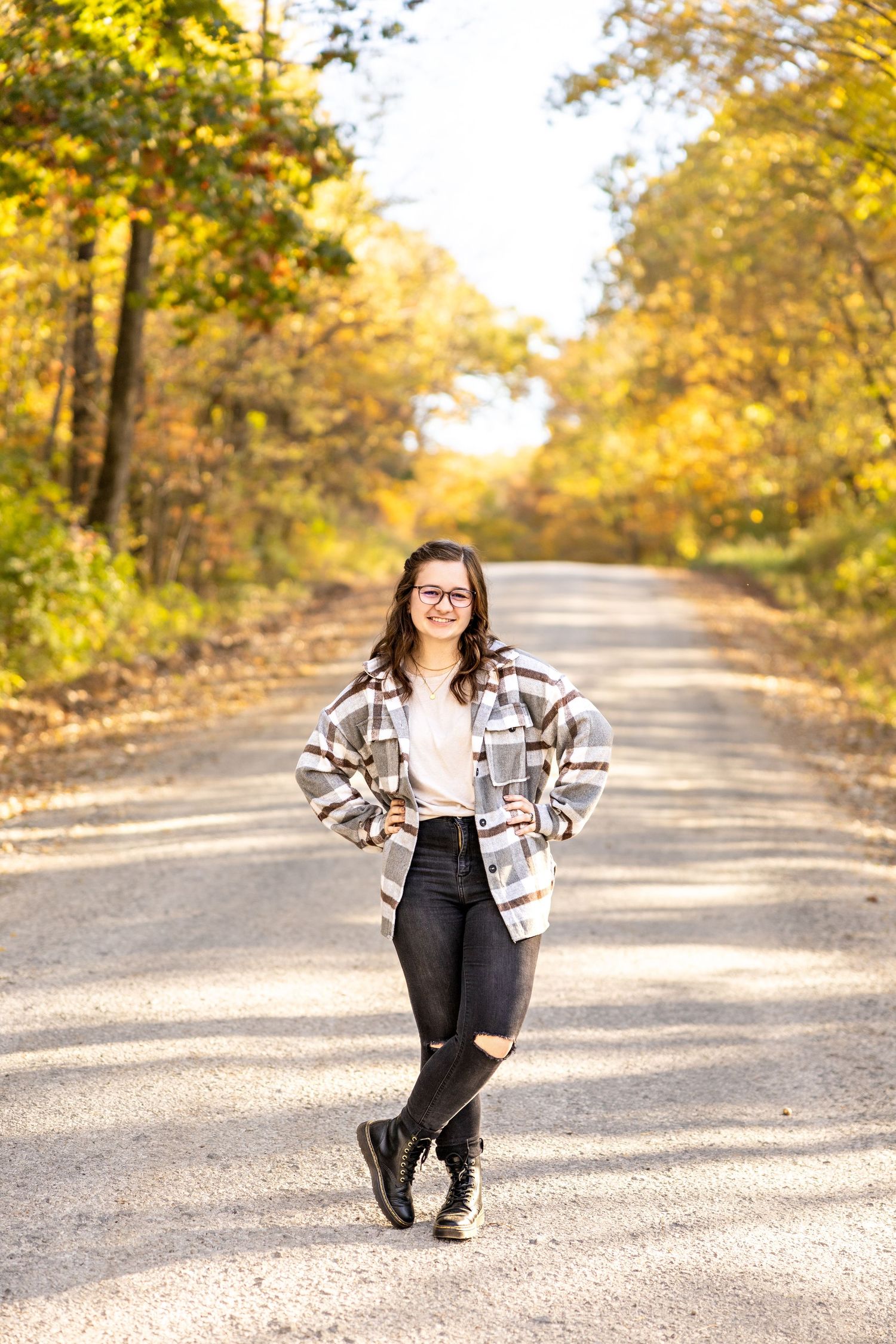 Casual fall fashion portrait on tree-lined path wearing plaid jacket and ripped jeans.