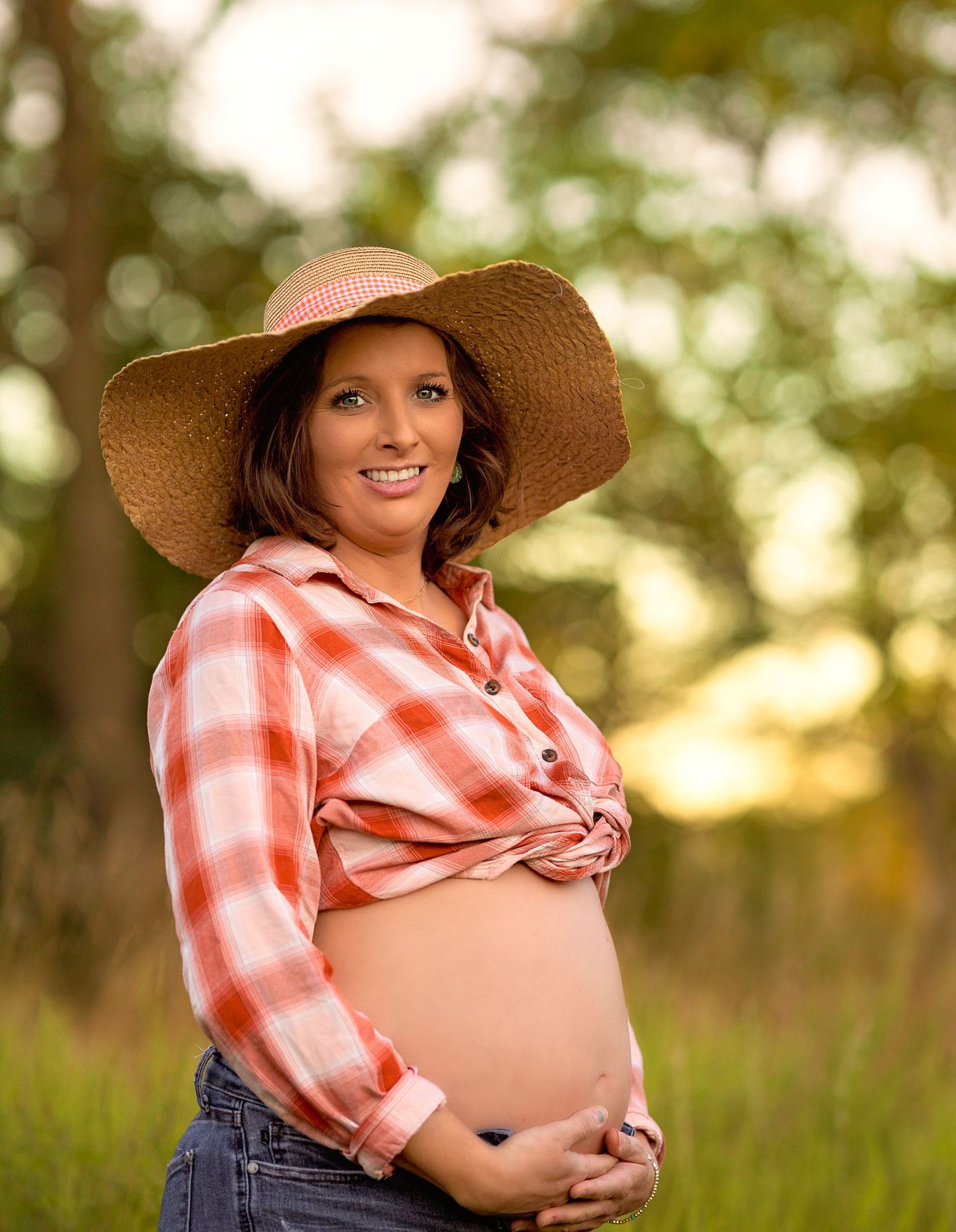 Maternity portrait featuring a plaid shirt, denim, and wide-brimmed hat in golden light.