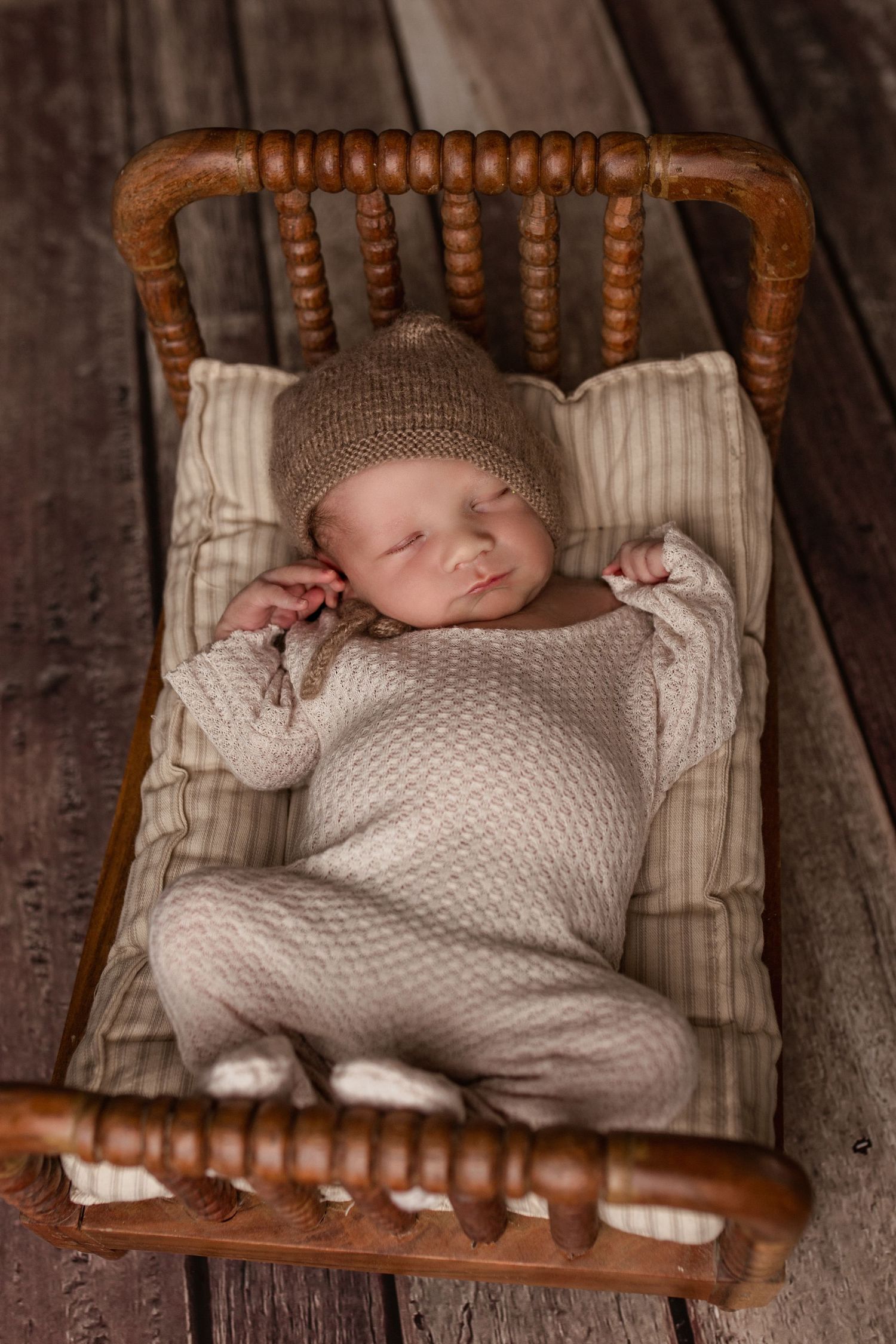 Peaceful newborn sleeping in vintage wooden crib wearing knit outfit.