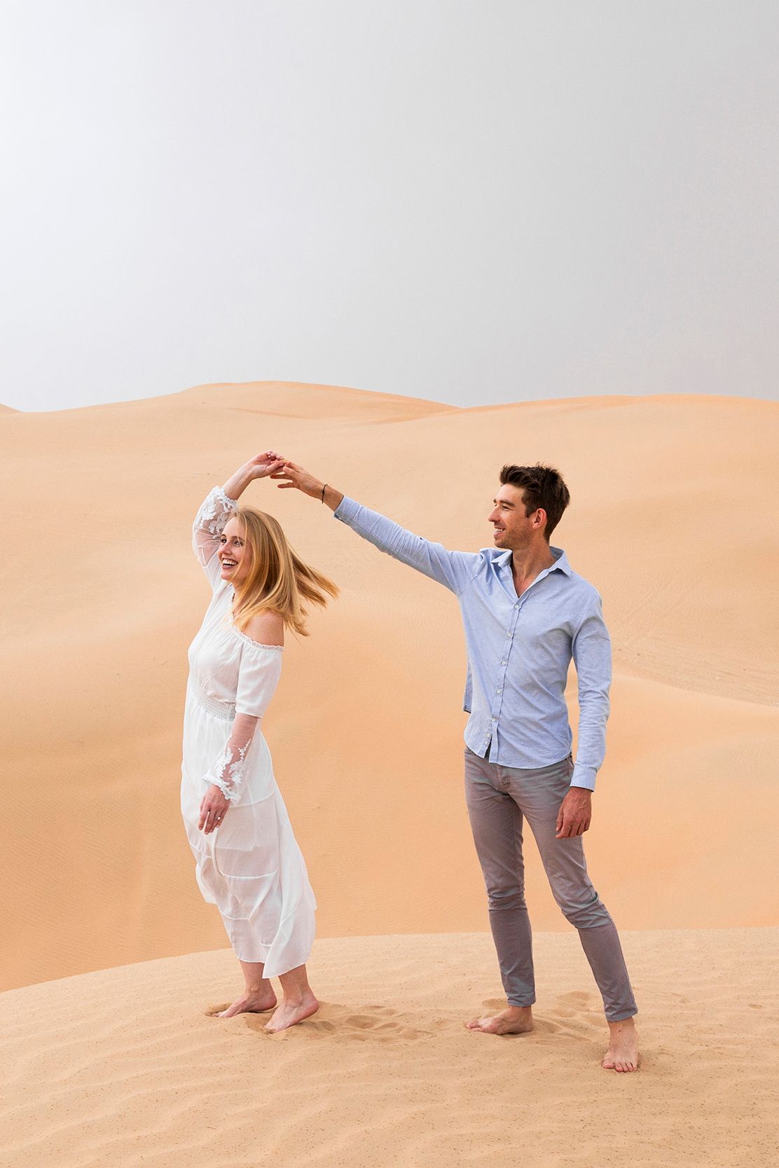 Couple playfully poses together against beautiful orange sand dunes in a desert setting.