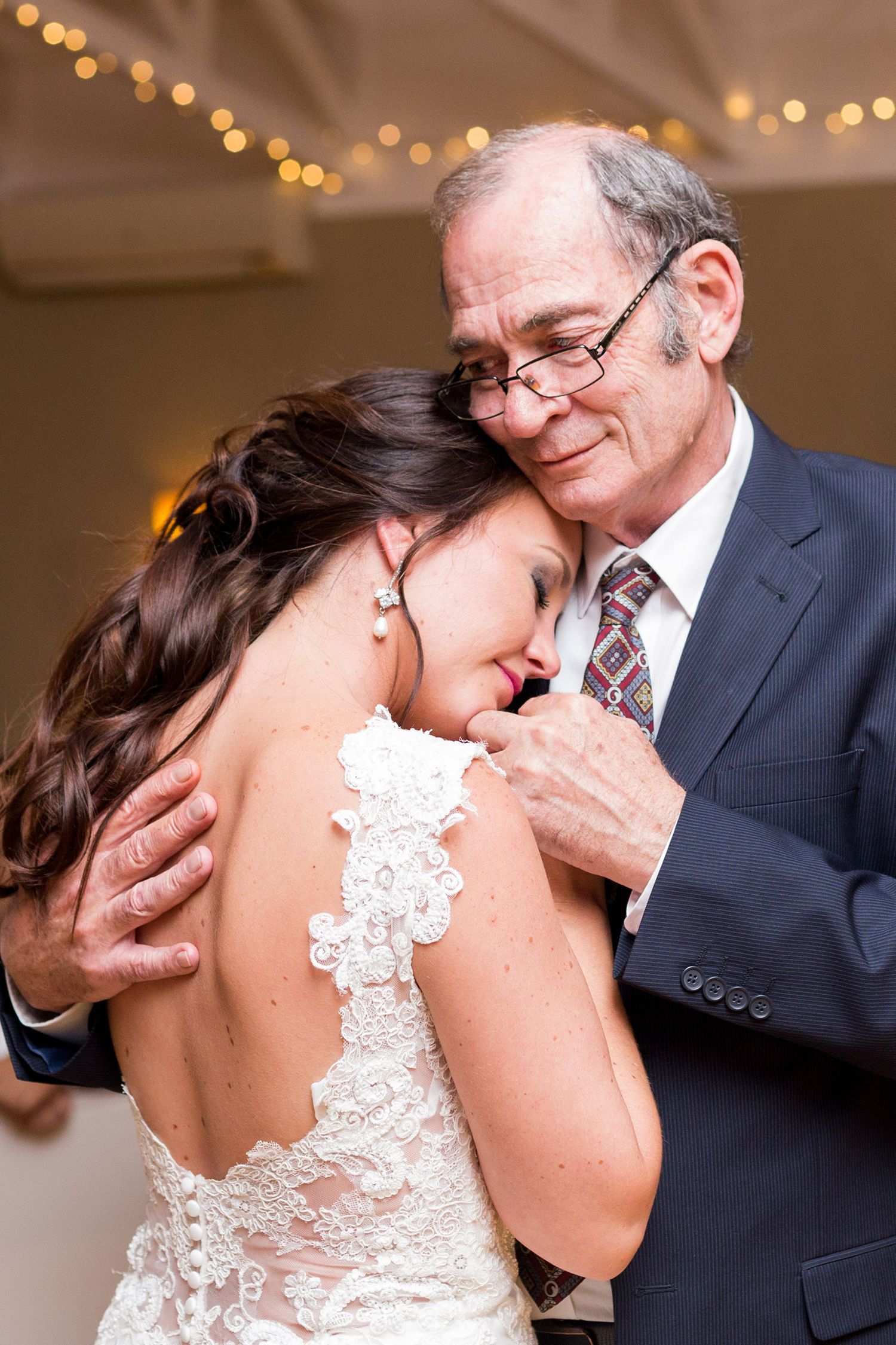 A tender emotional dance moment between a bride in a lace dress and an older guest at a wedding reception.