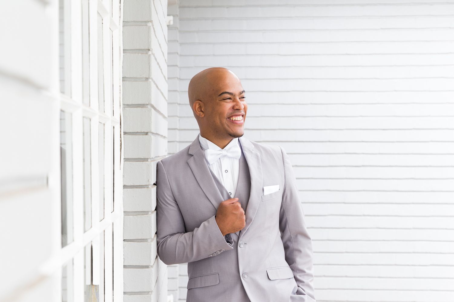 Professional wearing a light gray suit poses in front of white paneled wall for business portrait.