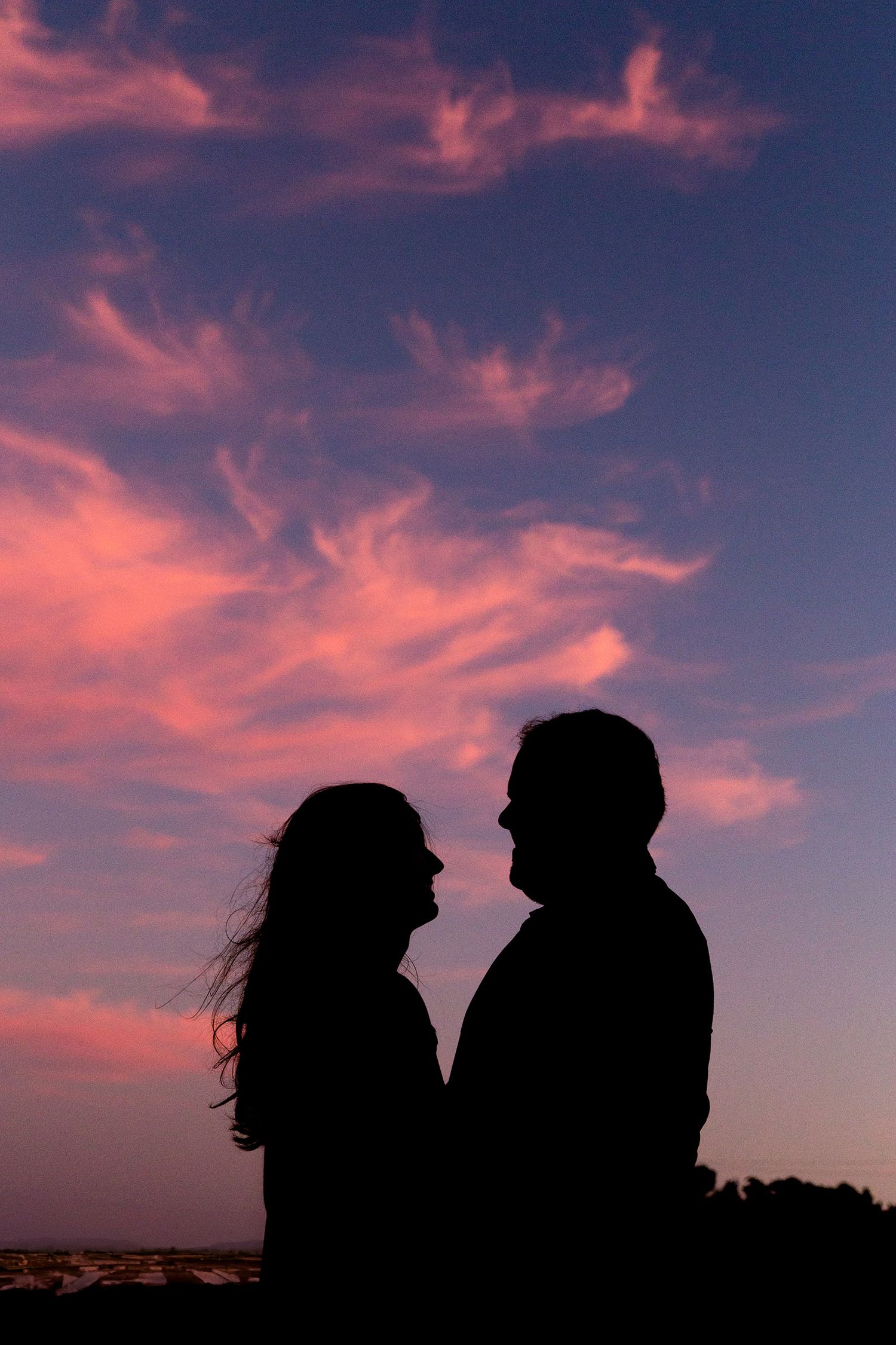 Silhouettes of two people against a dramatic pink and purple sunset sky with clouds.