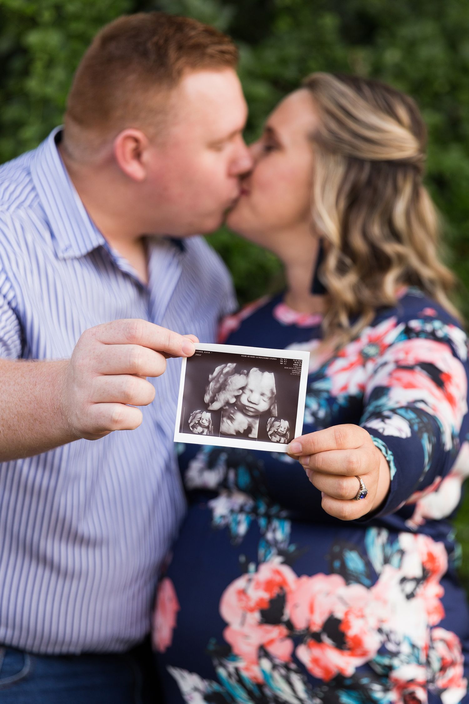 A couple shares a romantic moment while looking at photos in a garden setting during their maternity photo session.