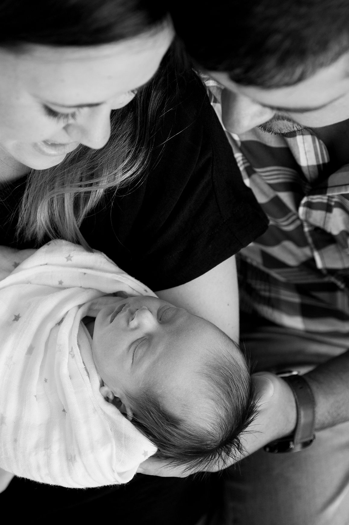 Black and white photo series showing tender moments between parents and their newborn baby in soft, intimate lighting.