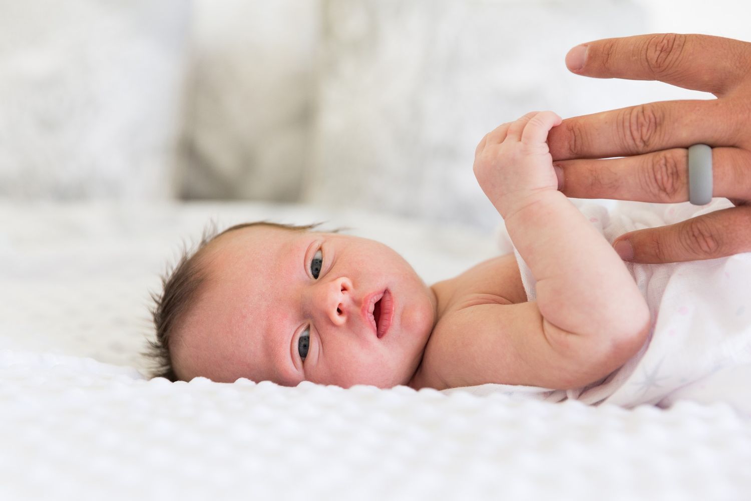 Baby lying on white blanket with various facial expressions showing sleepy, crying and happy moods in sequence.