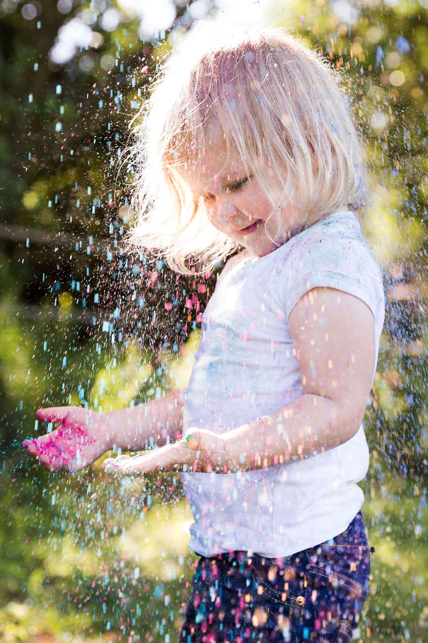 A playful scene of water droplets splashing in sunlight against a green outdoor background with floral elements.