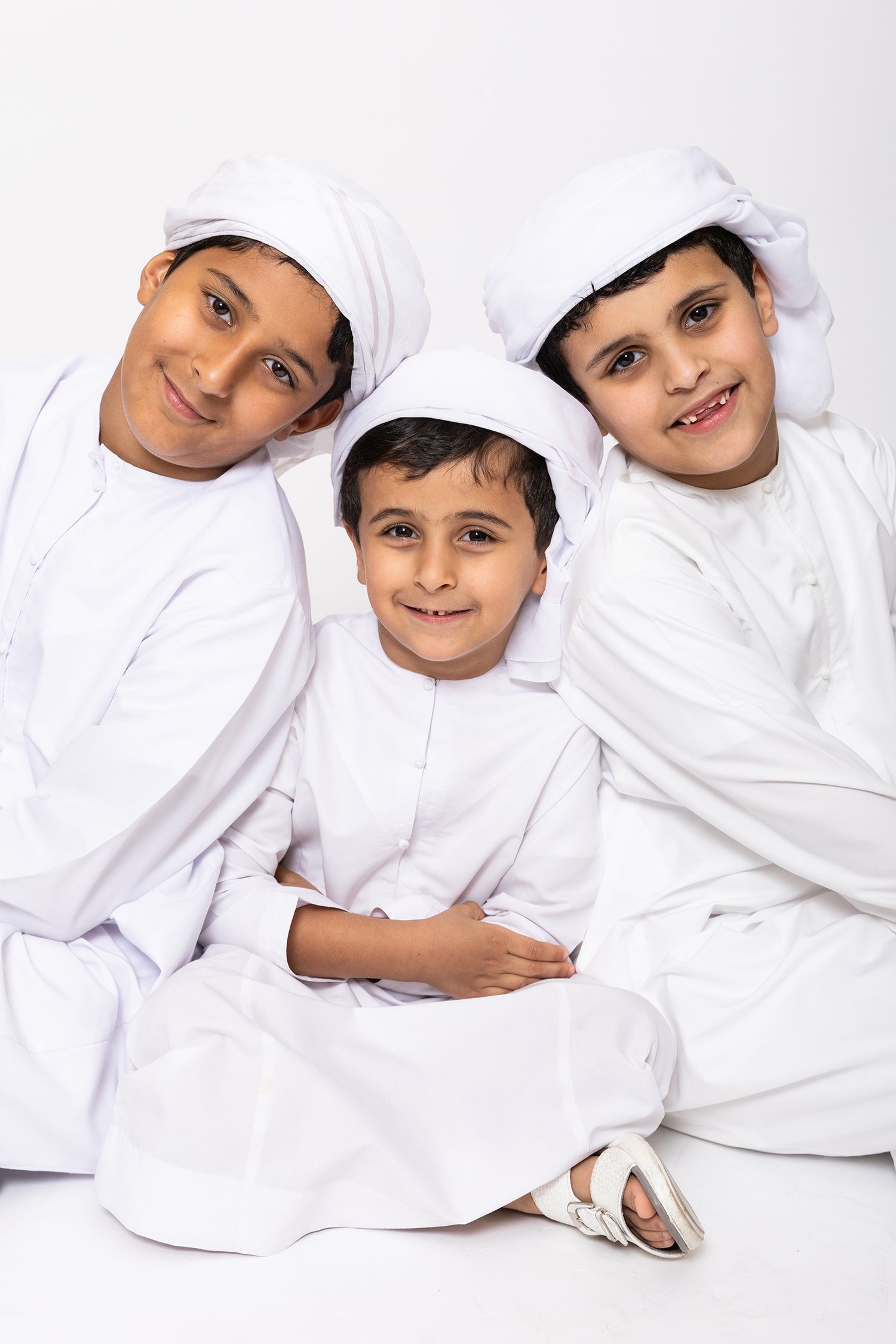 Children in traditional white Gulf Arab clothing laying down in line on white background.
