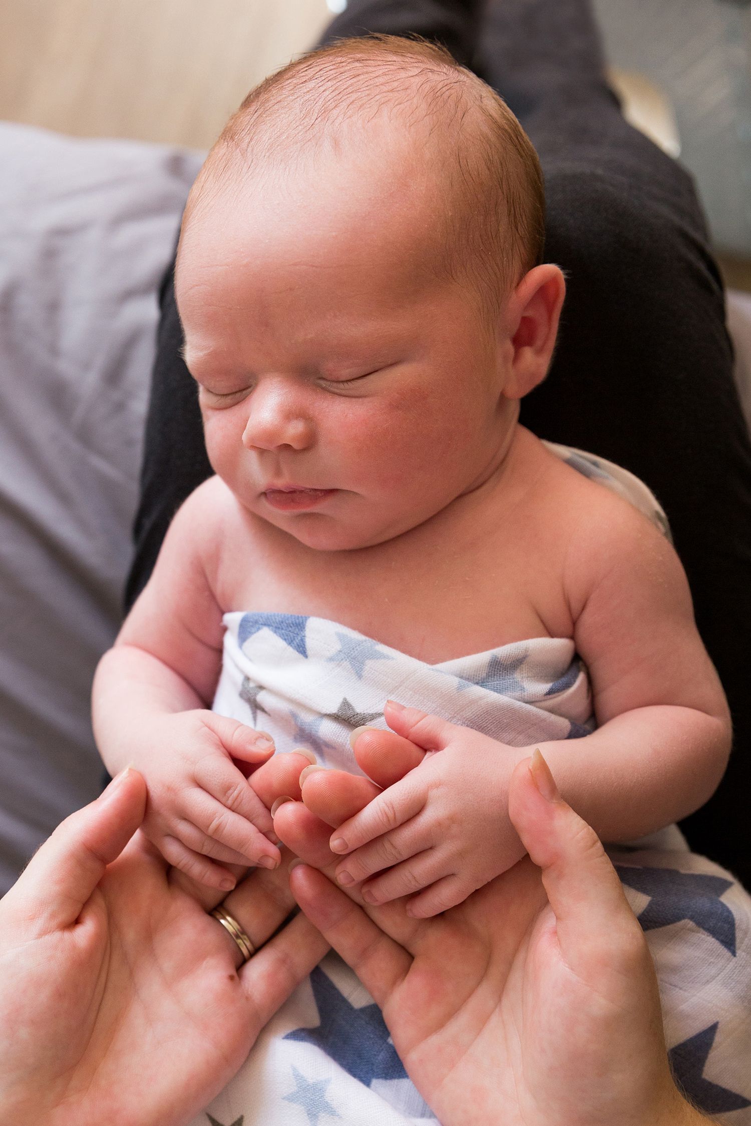 A sleeping newborn baby gently cradled in caring hands against a soft gray background.