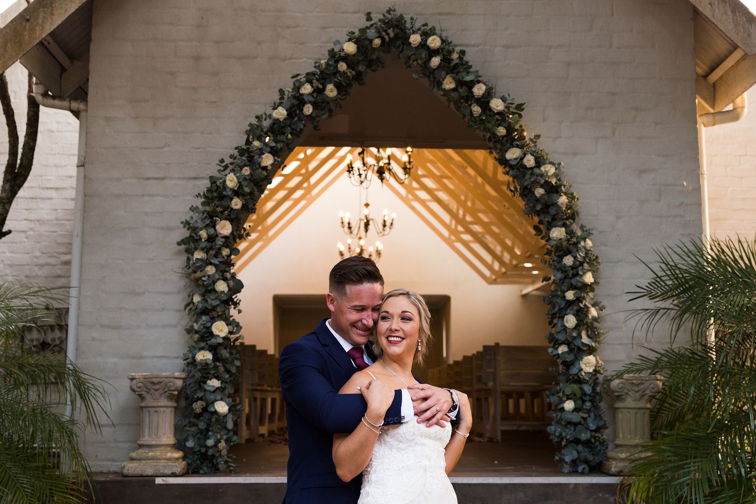 A couple in wedding attire stand close together under decorative holiday garland arches at their winter wedding celebration.