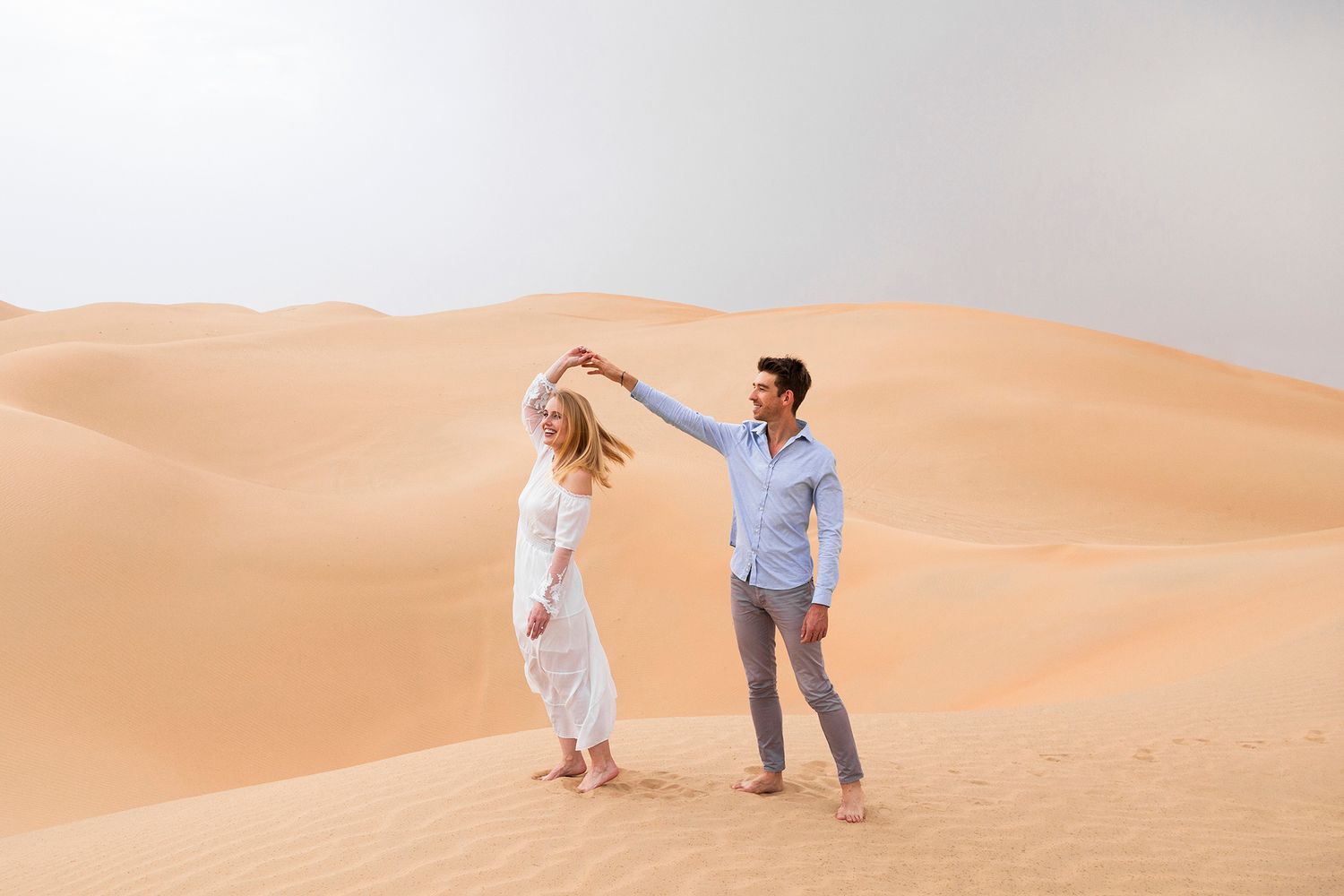 Two people walking through majestic sand dunes in desert landscape during sunset, creating long shadows.