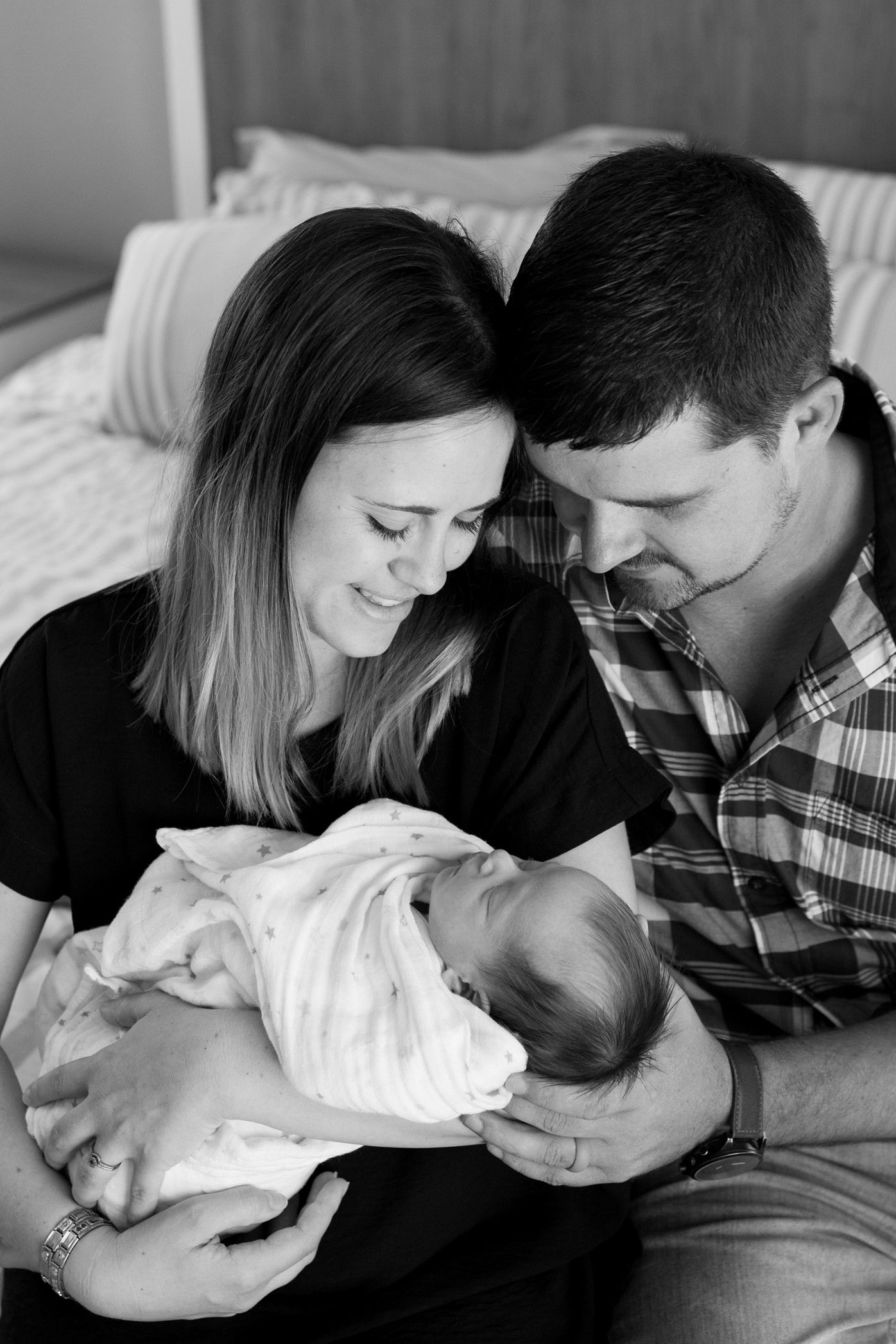 Black and white series of parents lovingly gazing at their newborn baby while resting on bed.