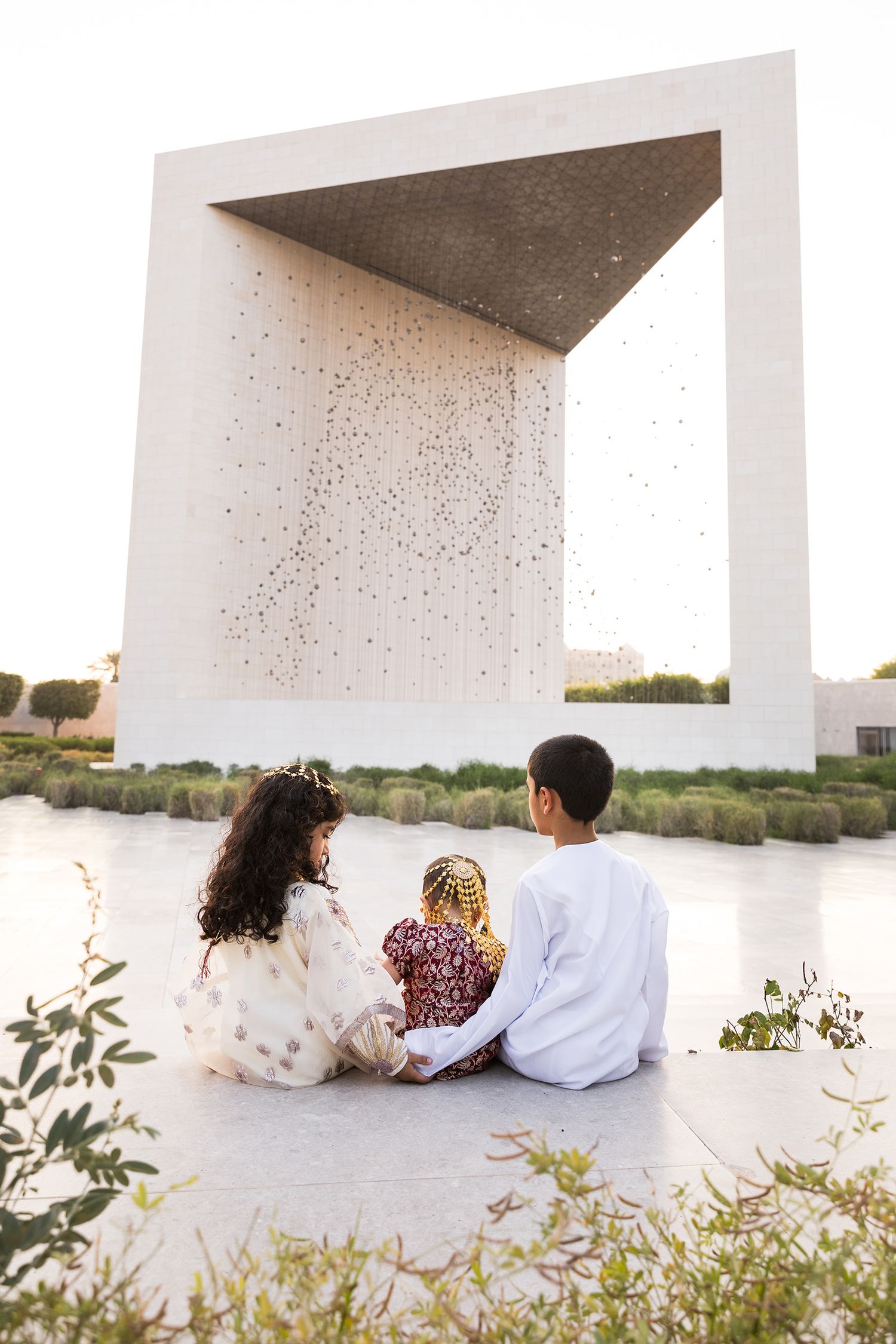 A family sits together at sunset near a modern white architectural structure overlooking calm waters.