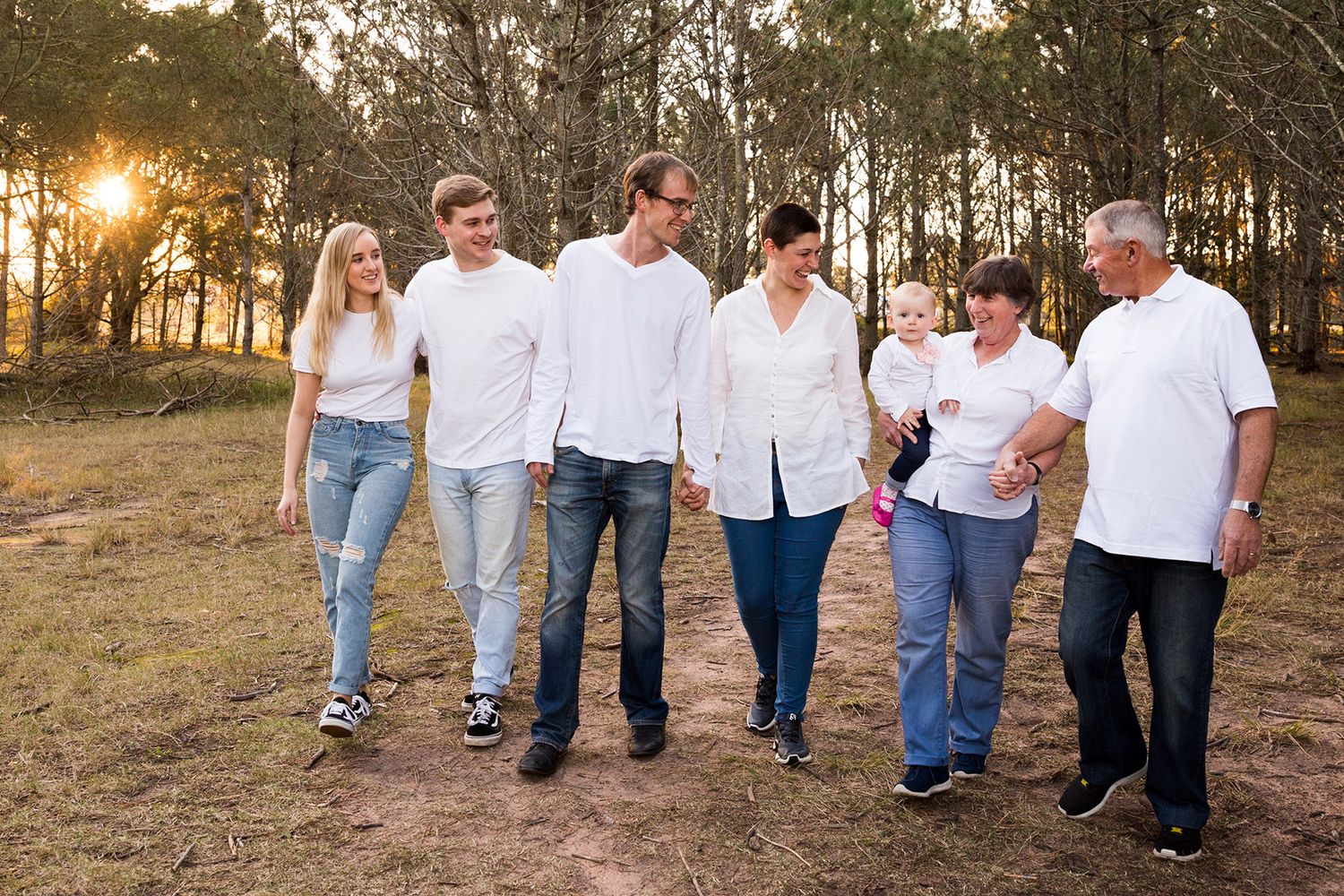 Group walking together in casual white shirts and jeans through a golden-lit outdoor setting at sunset.