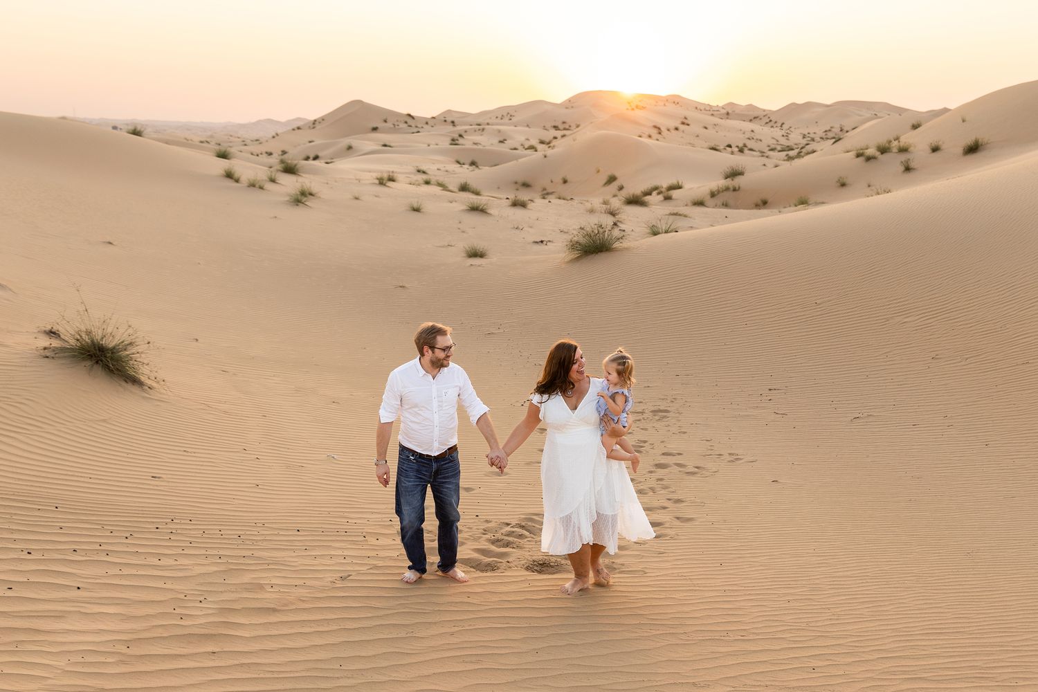 People walking together at sunset in sandy desert dunes with golden sunlight casting long shadows.