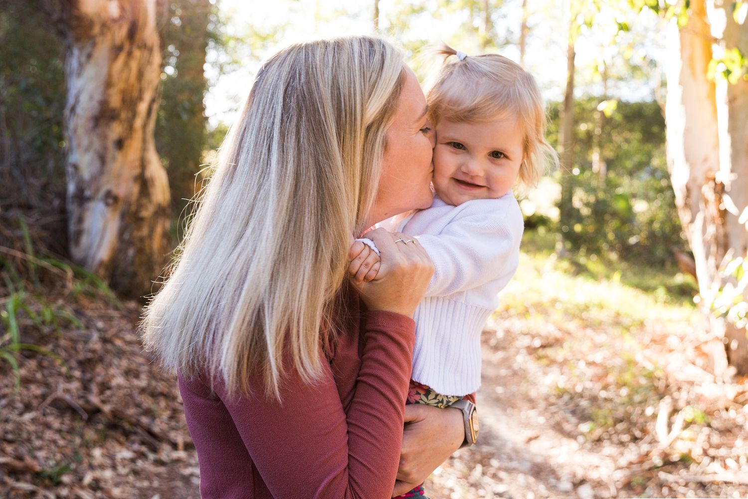 A series of warm, backlit photos showing tender moments between a parent and child in an outdoor forest setting.