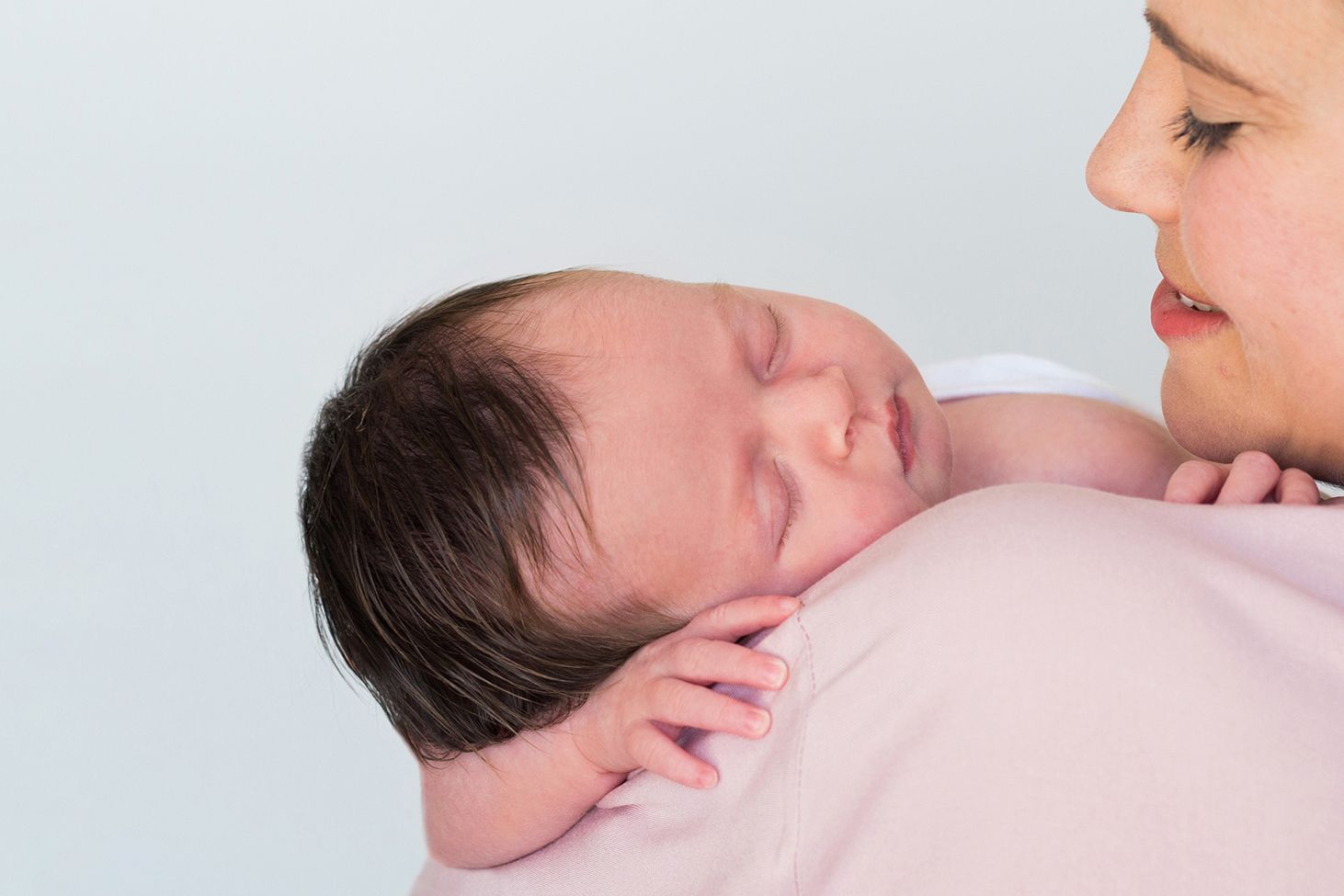 A newborn baby sleeps peacefully wrapped in white linens with soft pink tones.