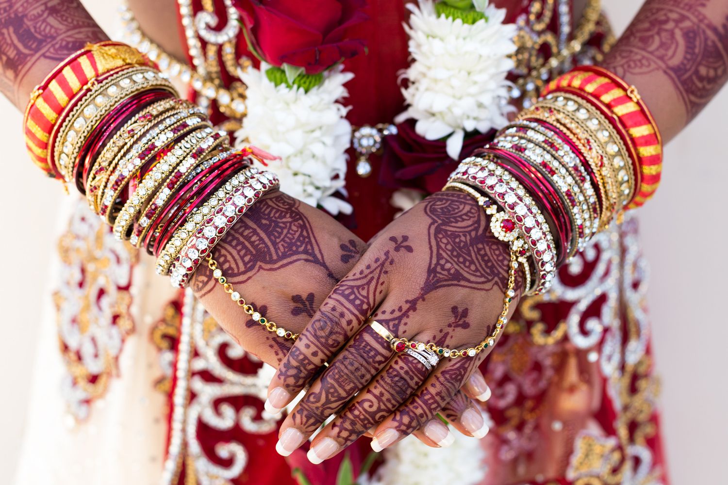 Traditional Indian bridal hands adorned with red and gold bangles, mehndi designs, and wedding jewelry.