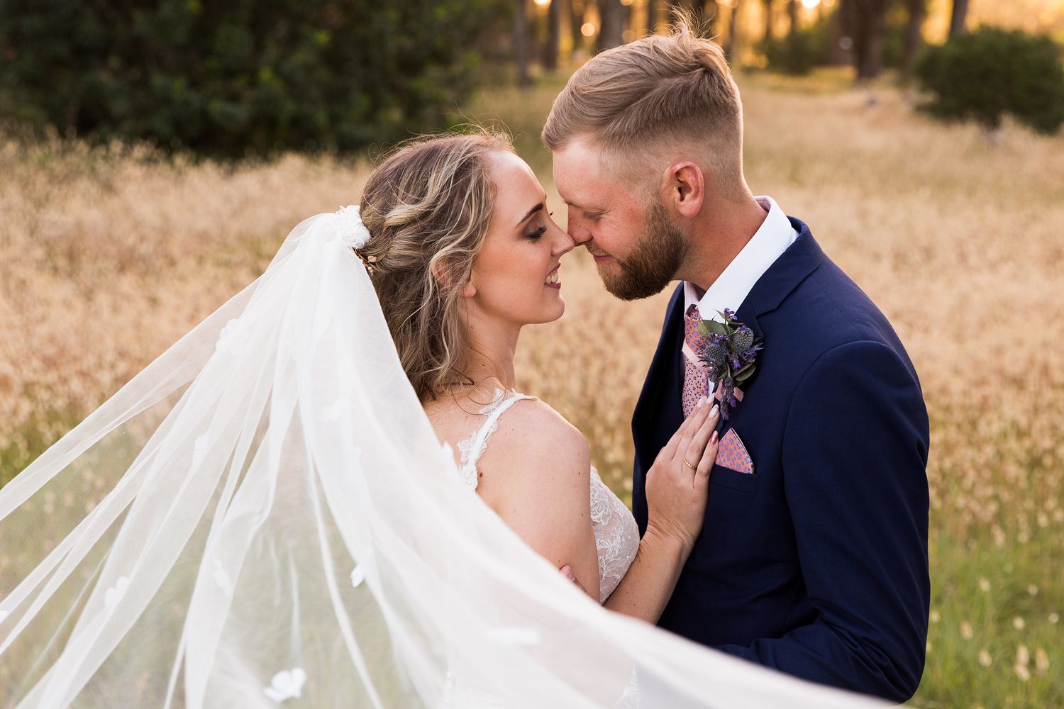 A romantic outdoor wedding photoshoot in a rustic field at golden hour shows tender moments between newlyweds.