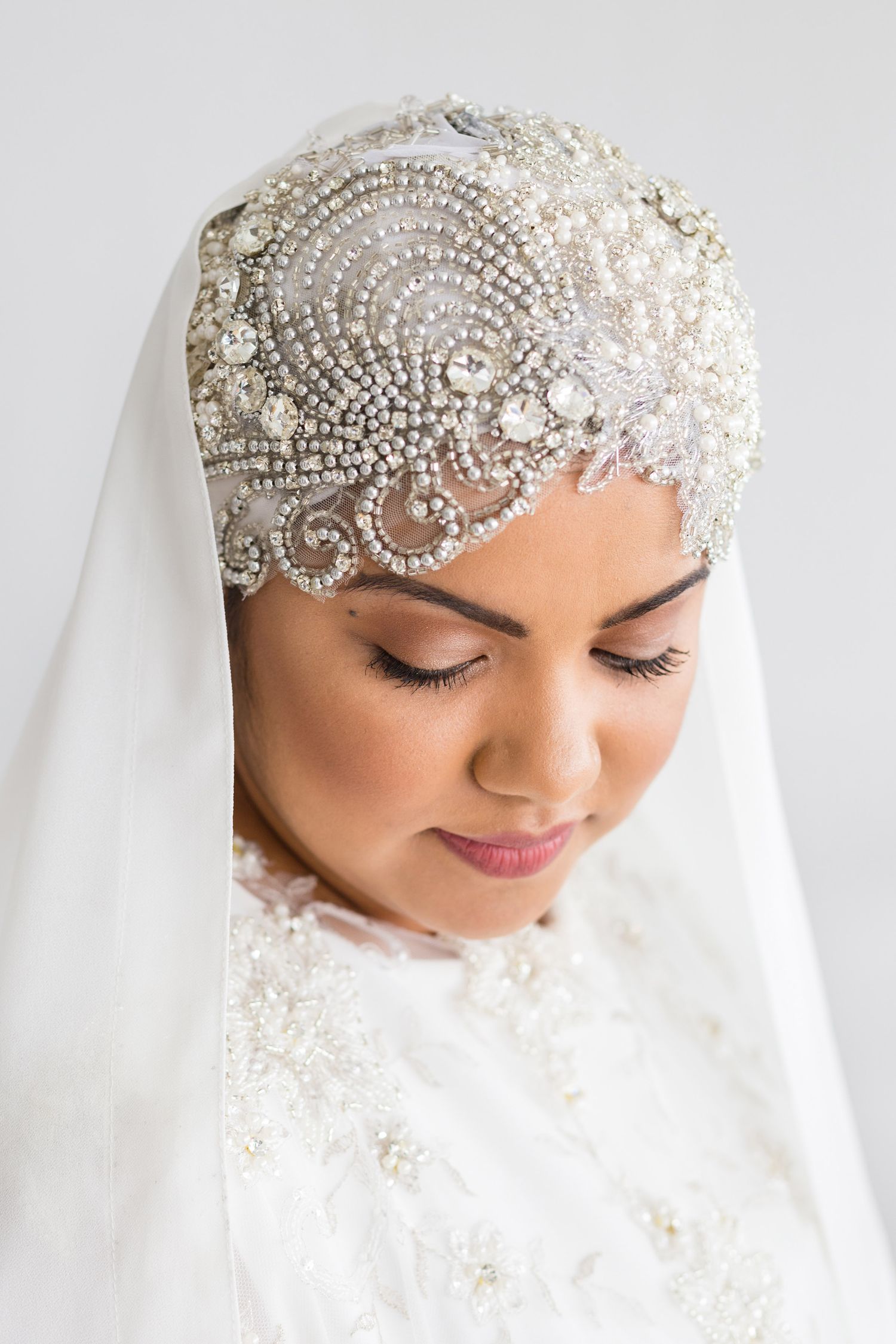 An elegant bridal veil features an ornate beaded crystal headpiece with swirling floral motifs against a white background.