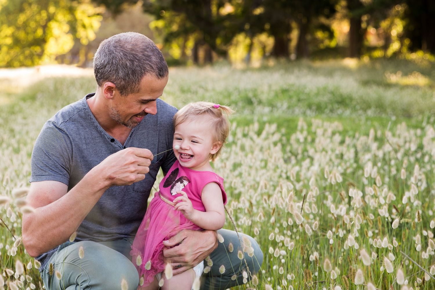 A playful candid sequence of a parent and child sitting together in a sunny grassy meadow during golden hour.