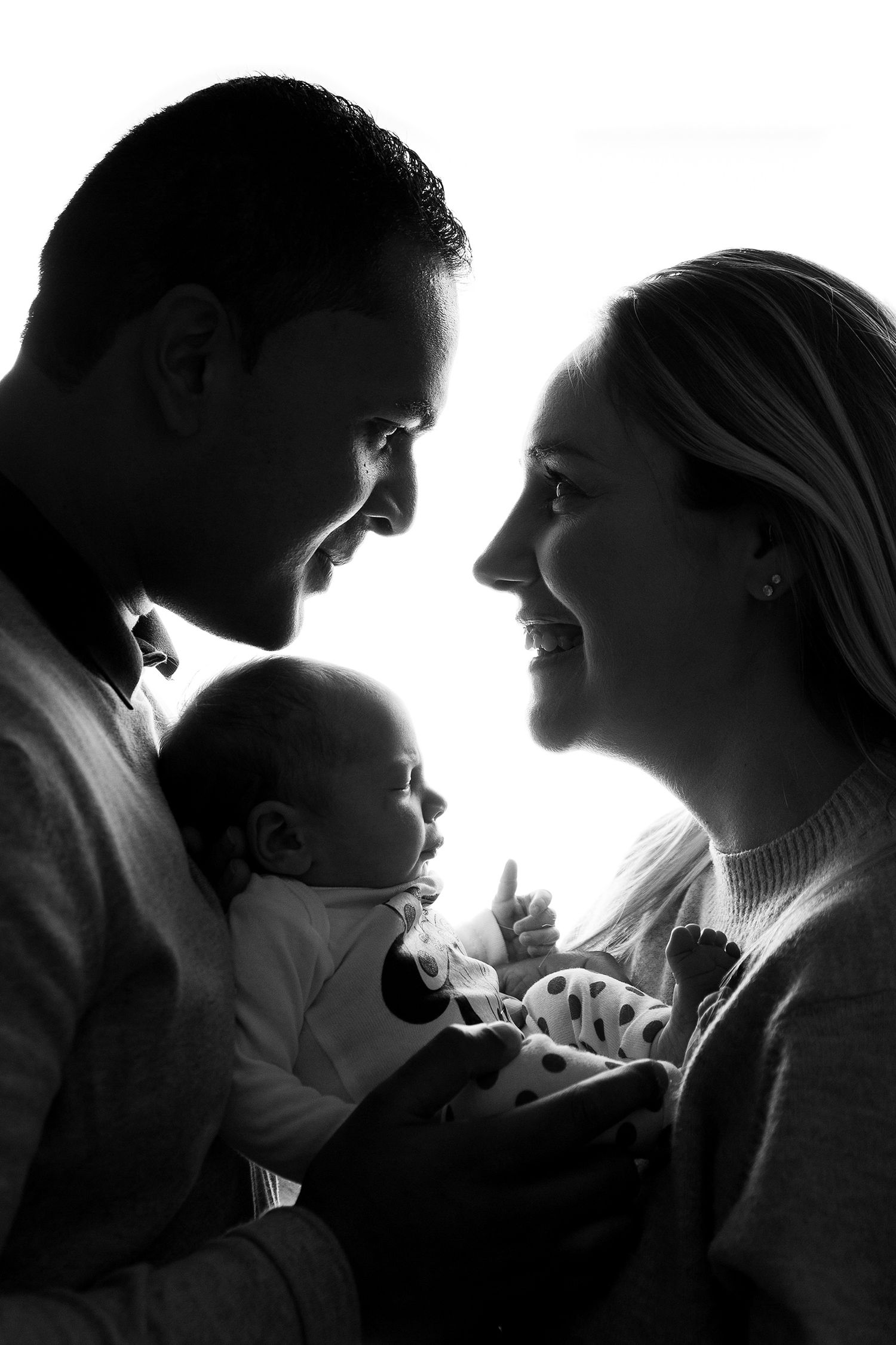 Black and white photo of smiling parents holding their newborn baby, sharing a tender family moment.