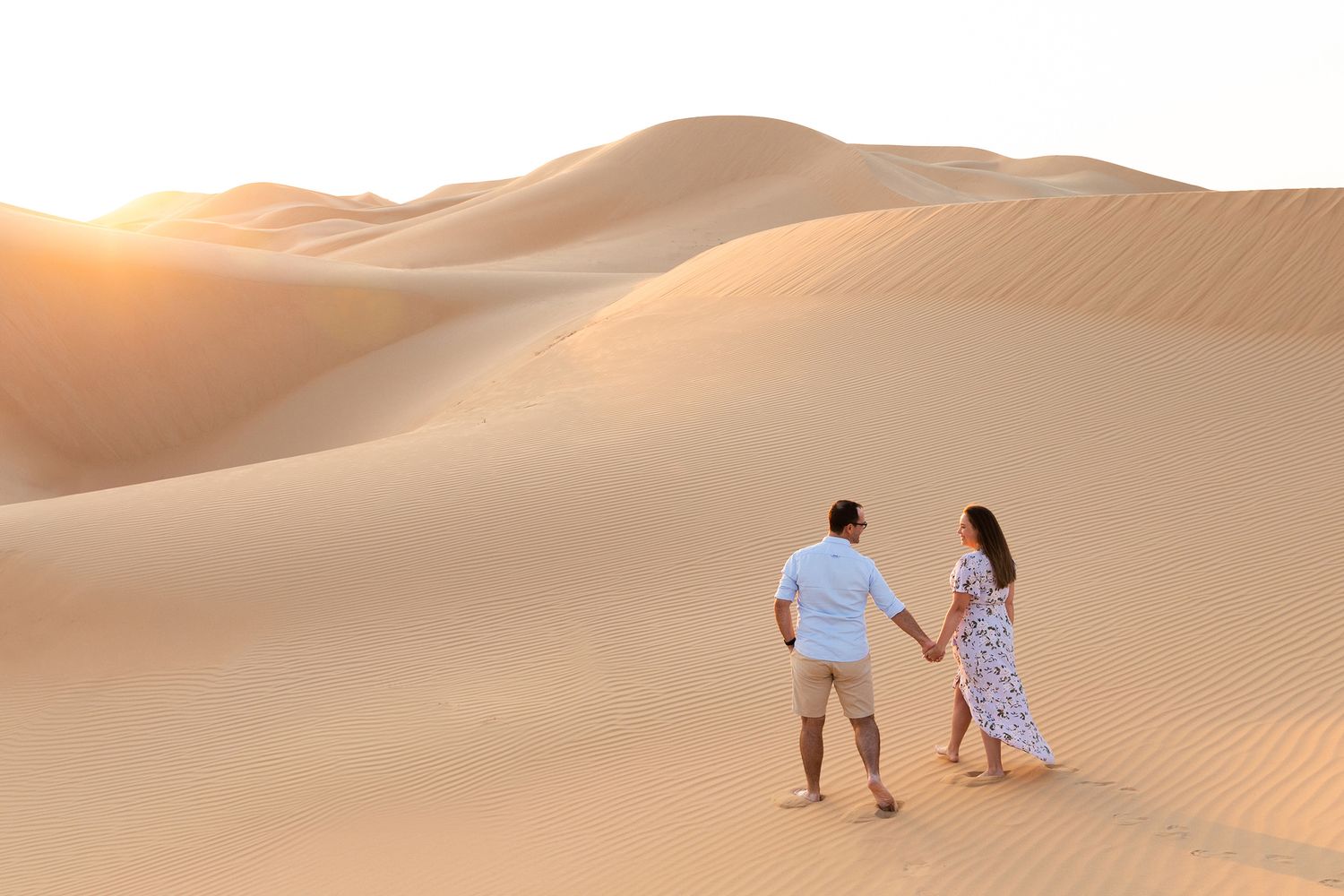 Couple silhouetted against a stunning desert sunset with rolling sand dunes in the background.