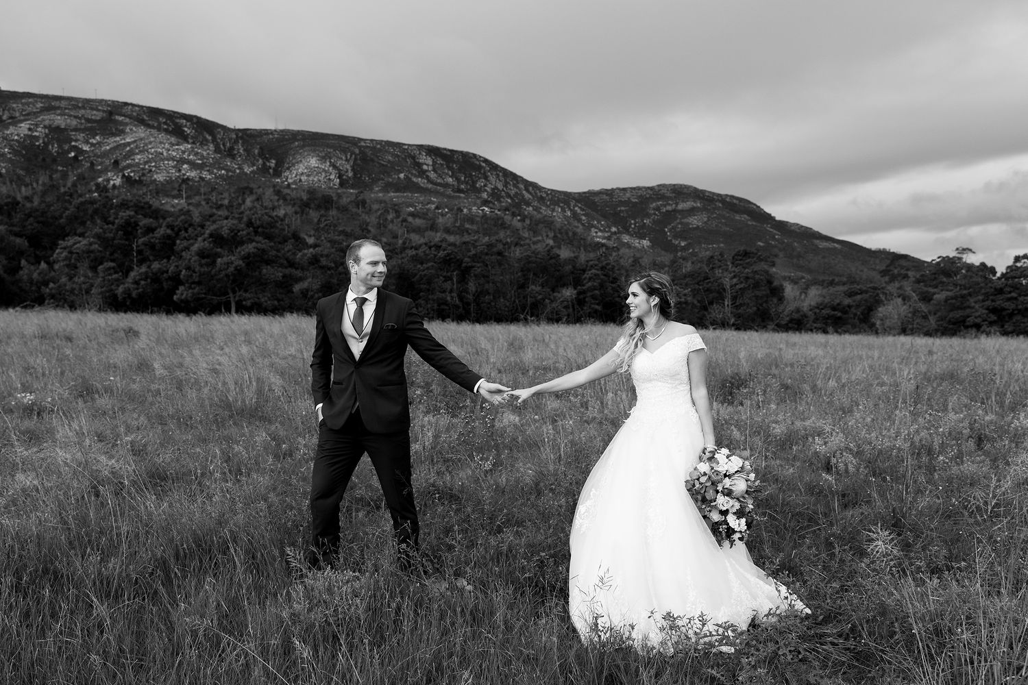 Romantic black and white wedding photo series of couple in field with mountains in background.