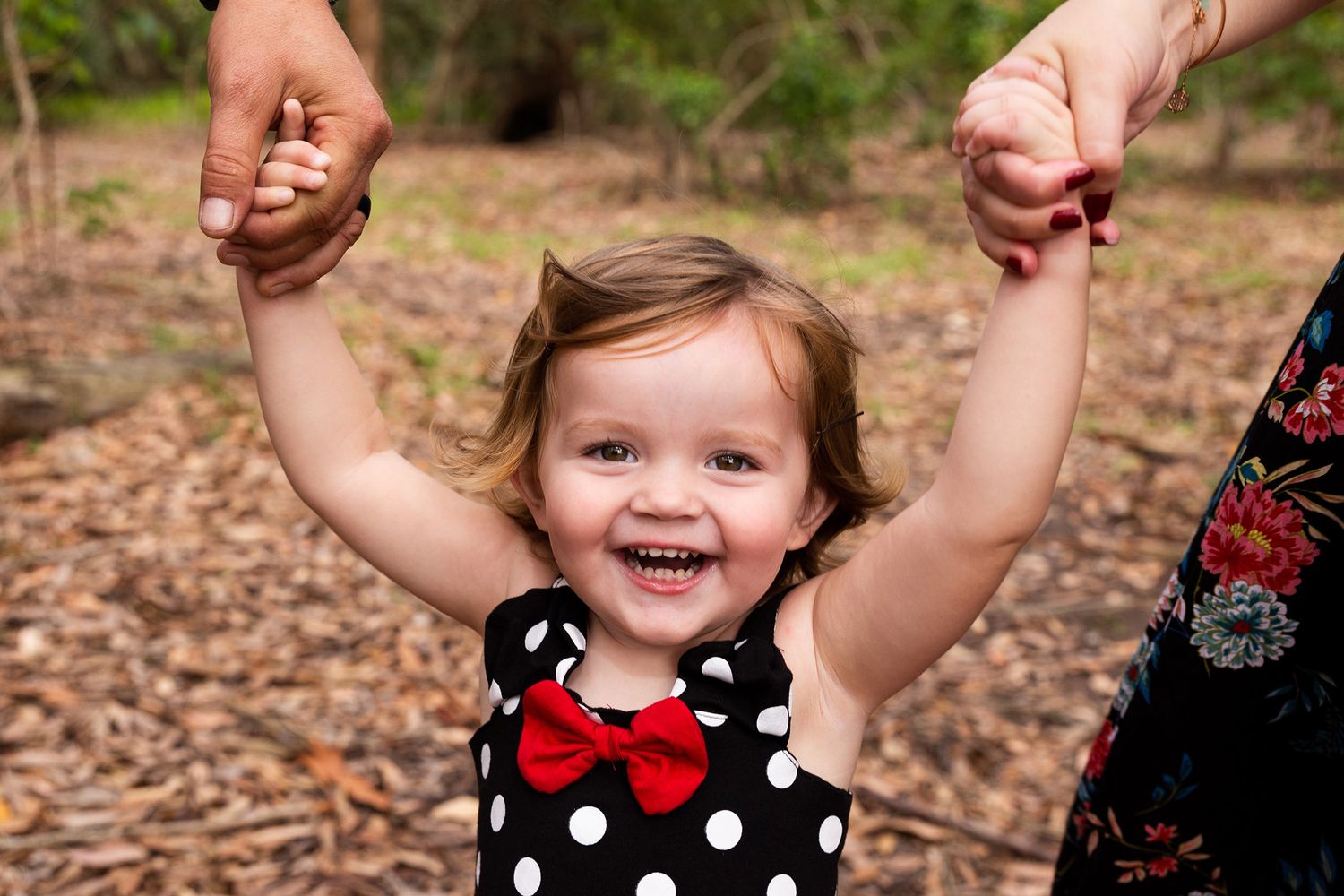A child in a black and white polka dot dress holds hands with someone while playing outdoors in an autumn setting.