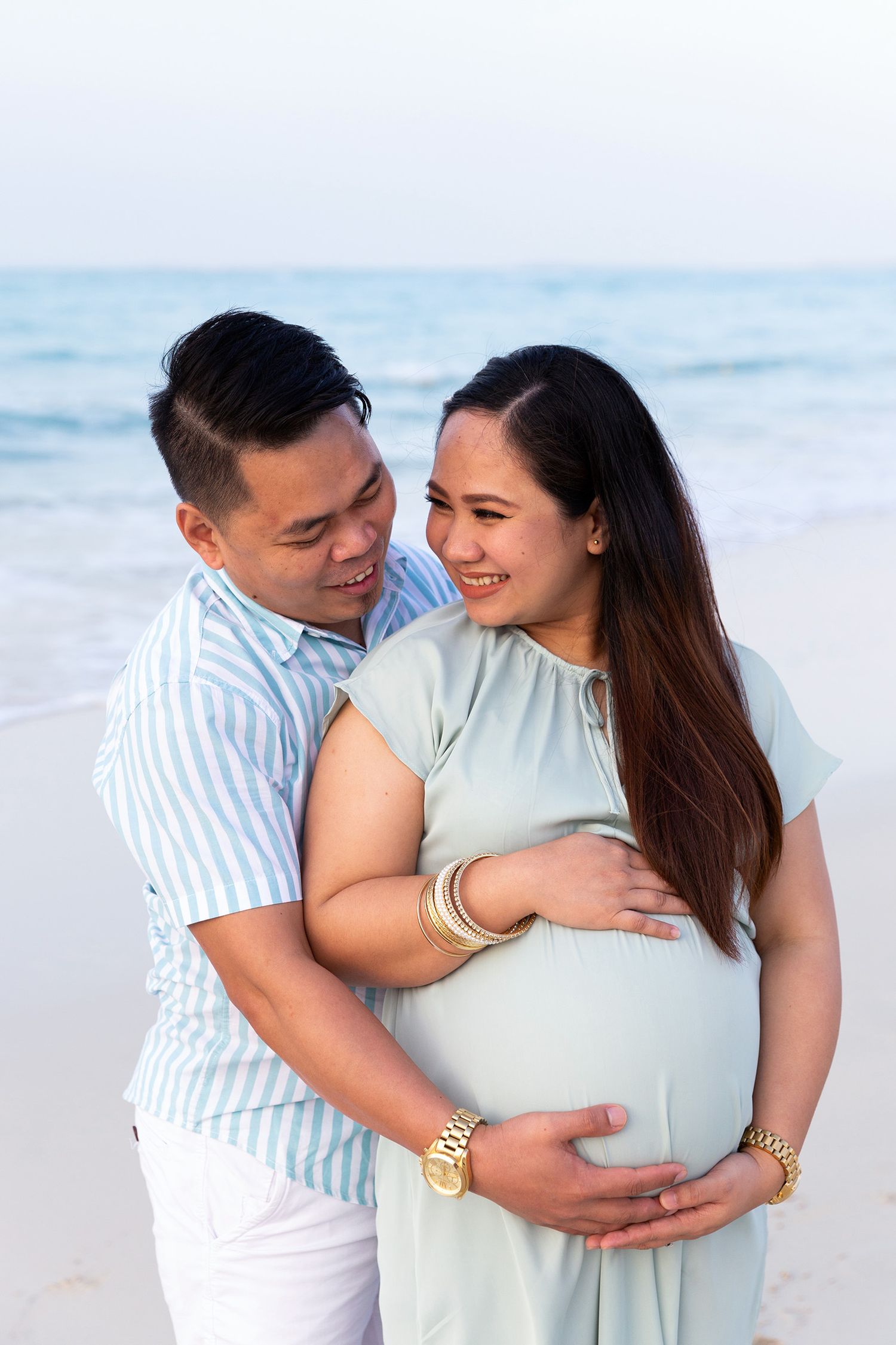 Romantic couple embraces while standing on a beautiful beach with white sand and ocean views at sunset.