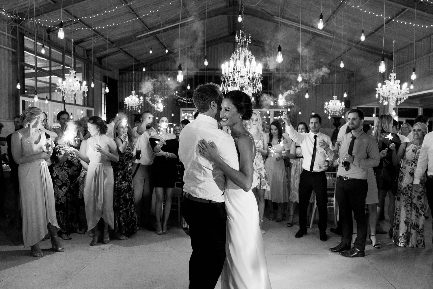 Couples dancing and celebrating at an elegant wedding reception with chandeliers and string lights decorating the venue.