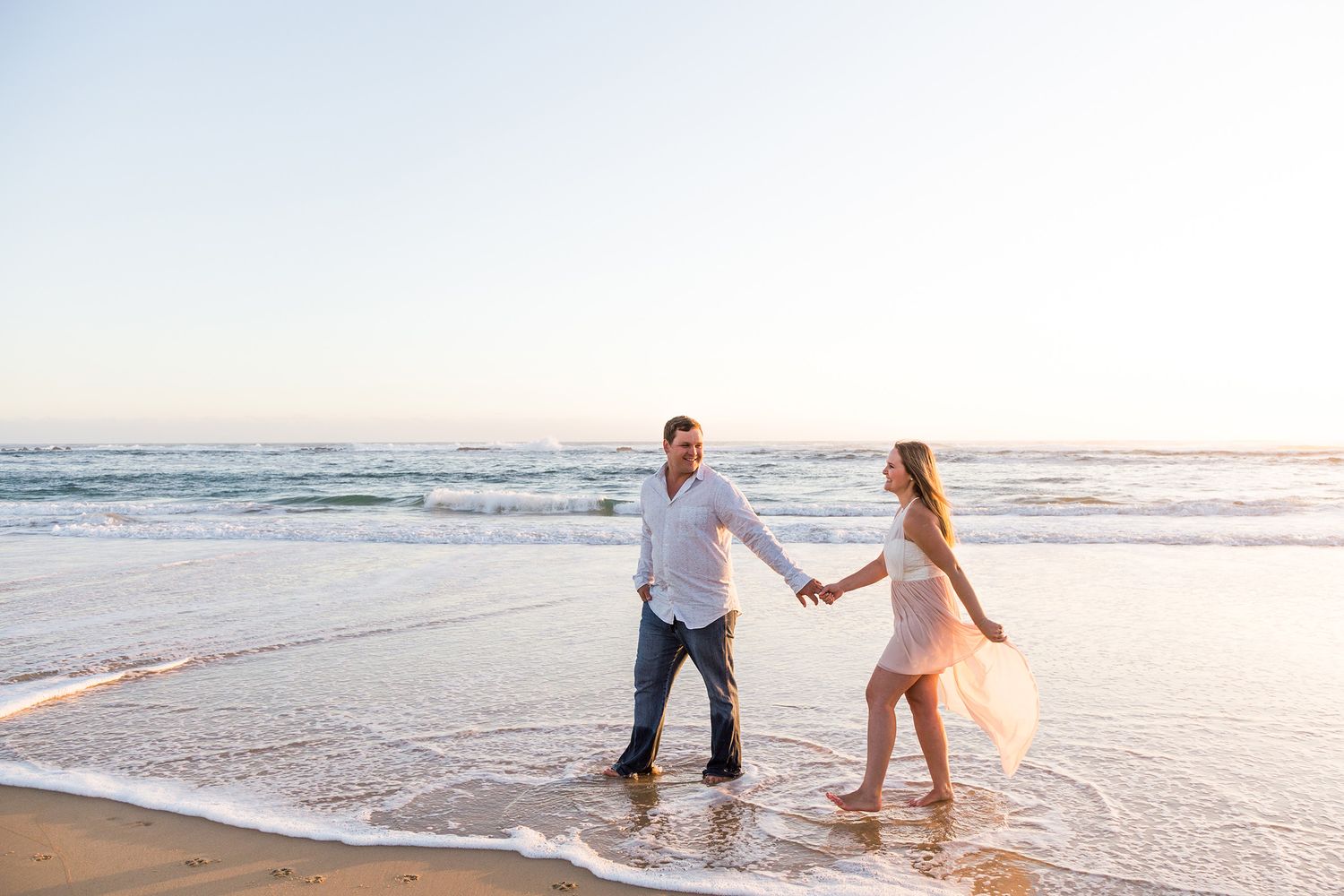 Couple holding hands and walking together on a scenic beach during golden hour.