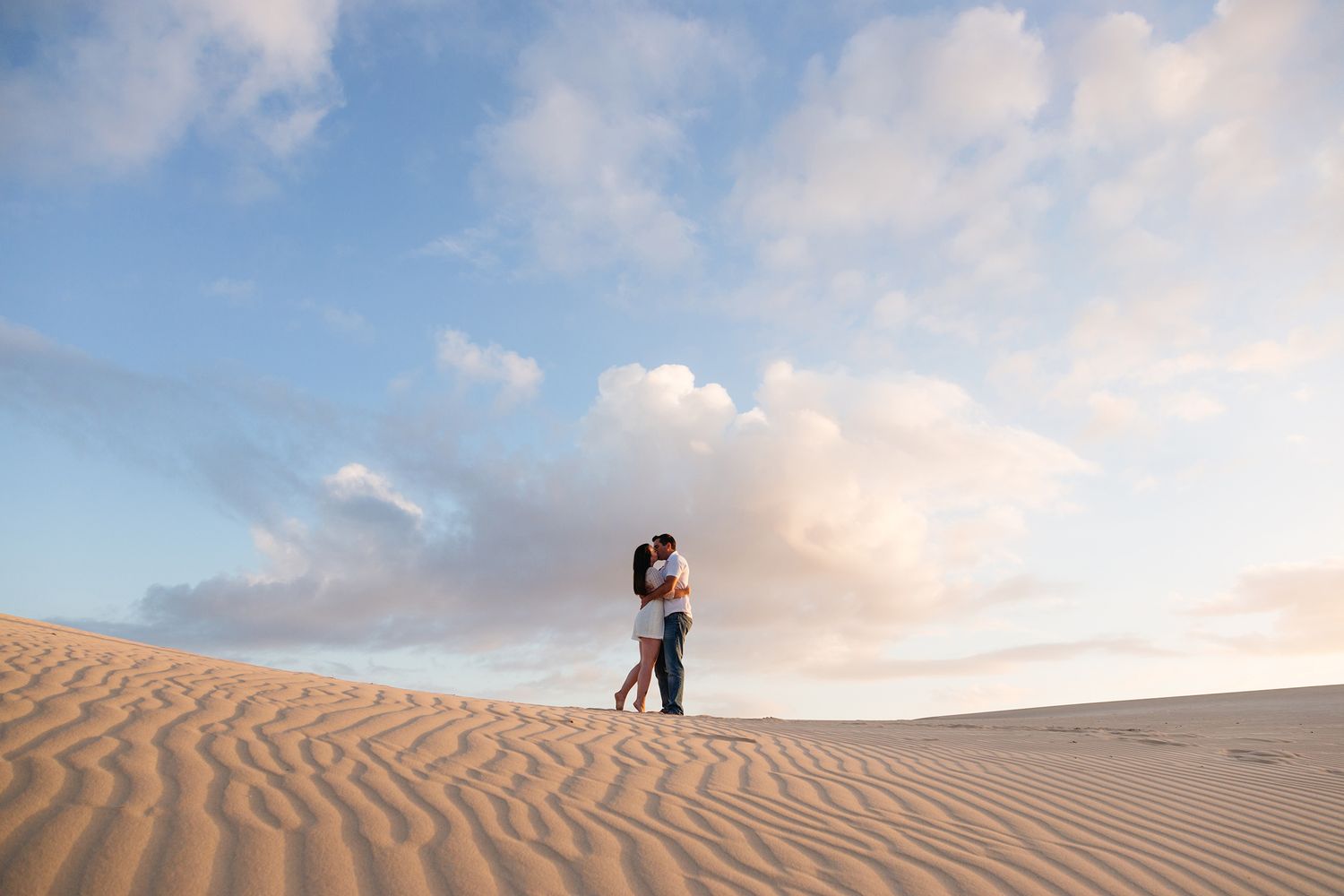 People walking and enjoying leisure time on scenic rolling sand dunes under a bright cloudy sky.