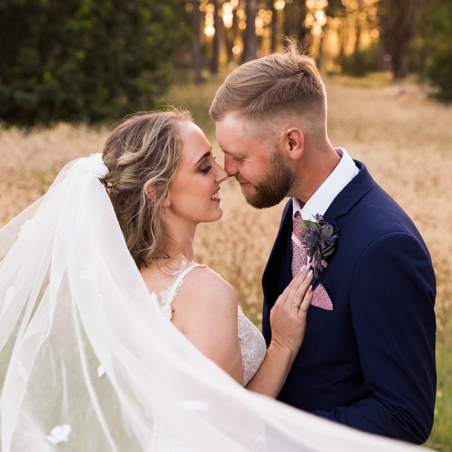 A romantic wedding couple shares an intimate moment in golden sunlight beneath a flowing white veil.