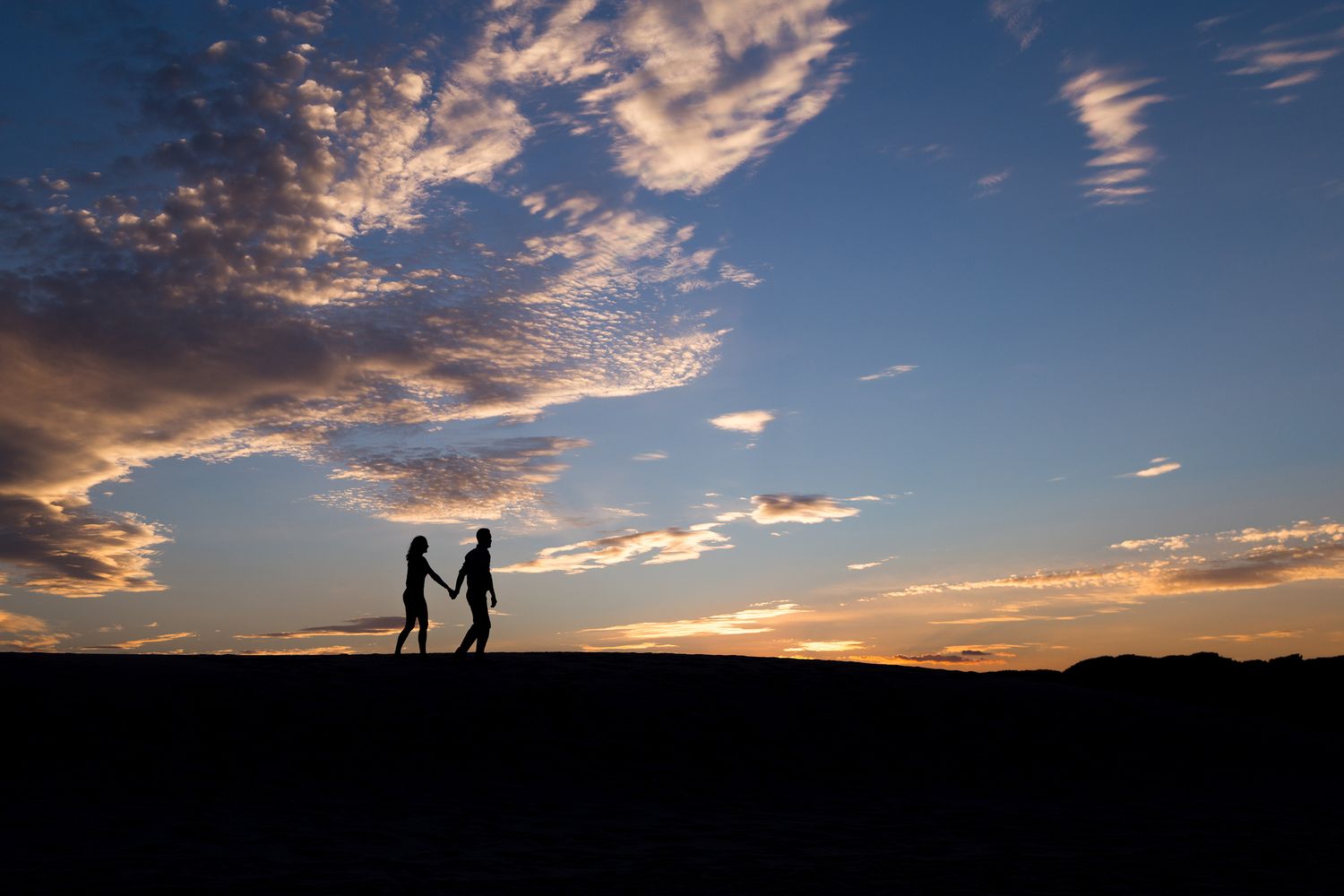Silhouettes of people walking along a hill against a dramatic sunset sky with streaking clouds.