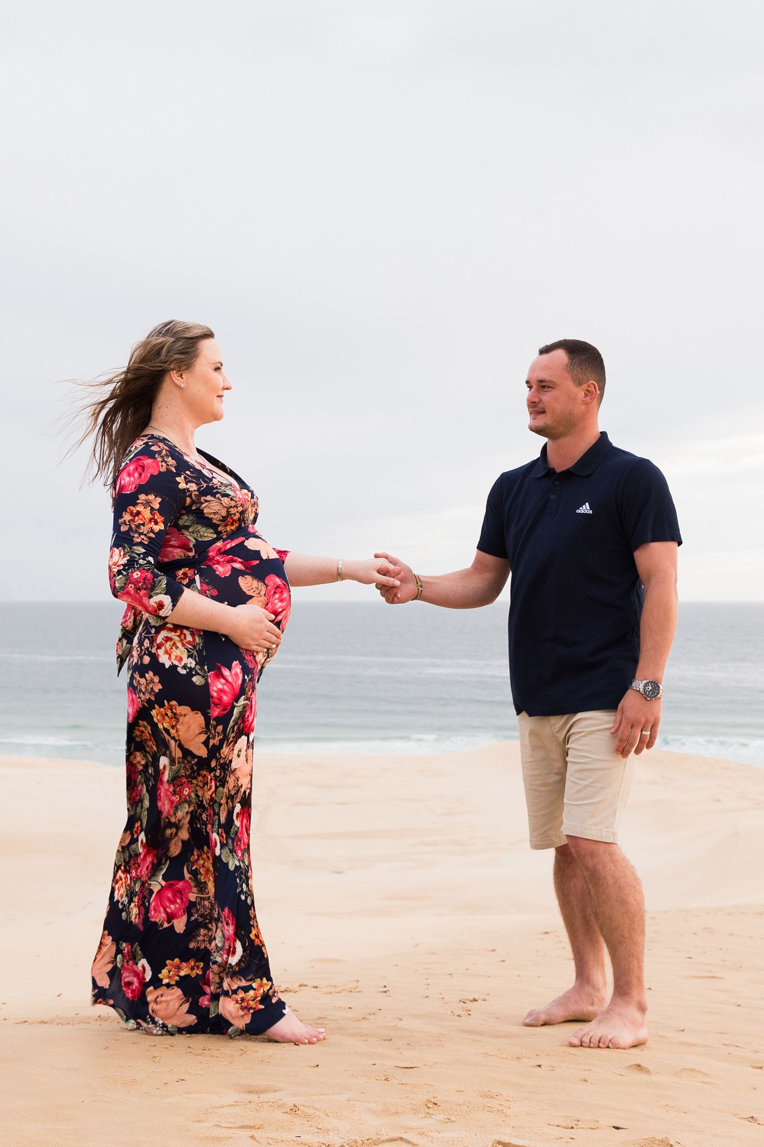 A couple twirls in a playful dance together on a sandy beach with the ocean in the background.