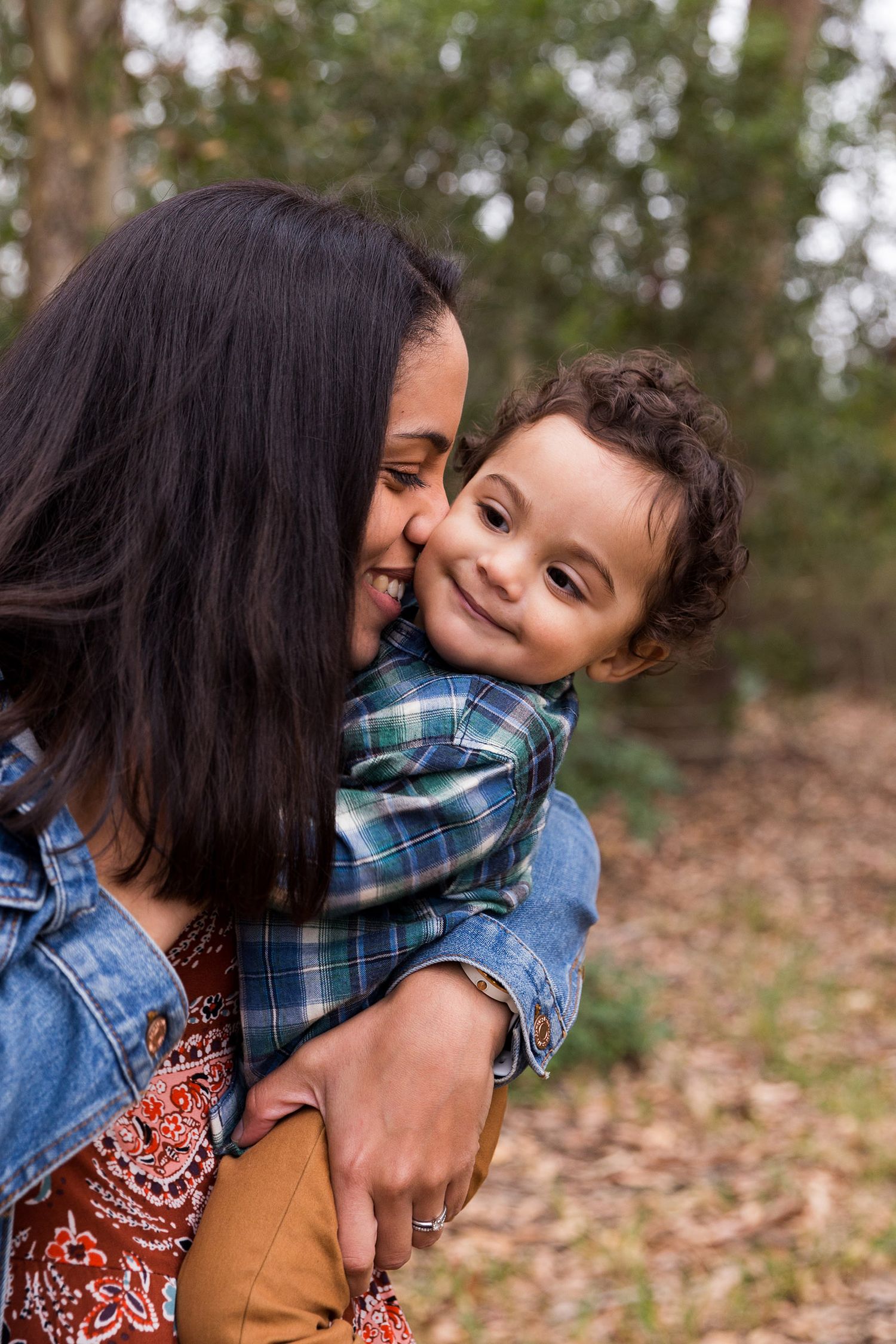 A tender moment between a parent and child in plaid clothing against a natural outdoor backdrop.